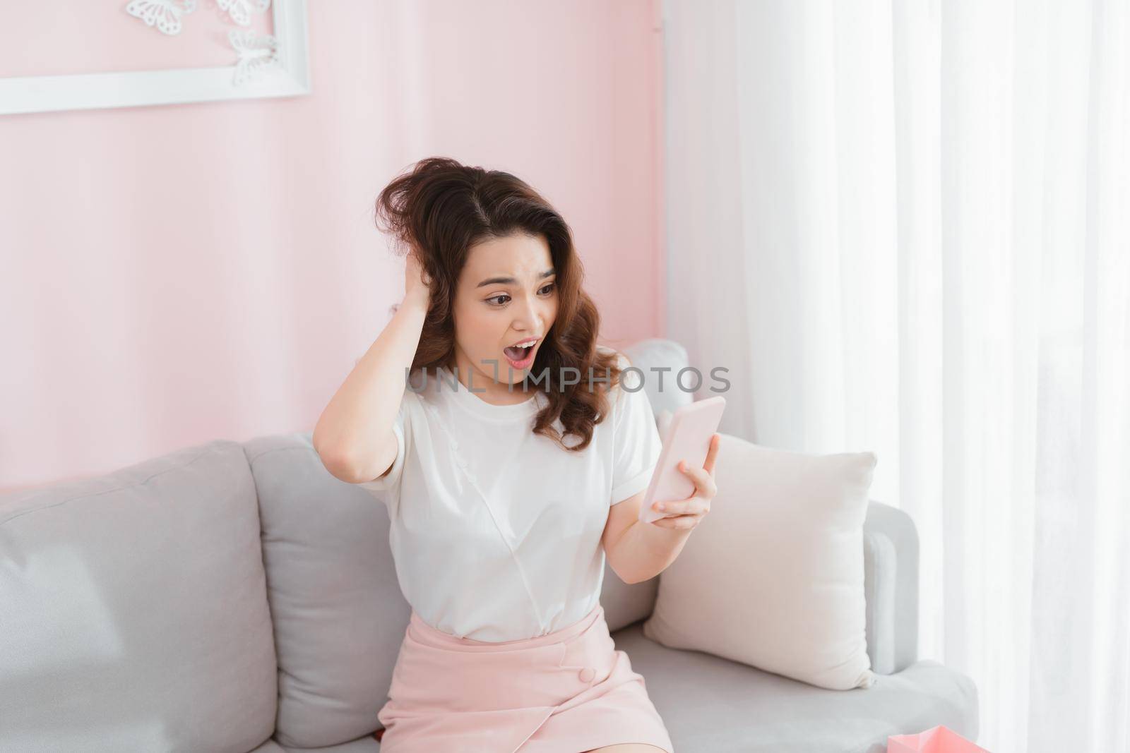 Asian woman reading shocking text at home in the living room by makidotvn