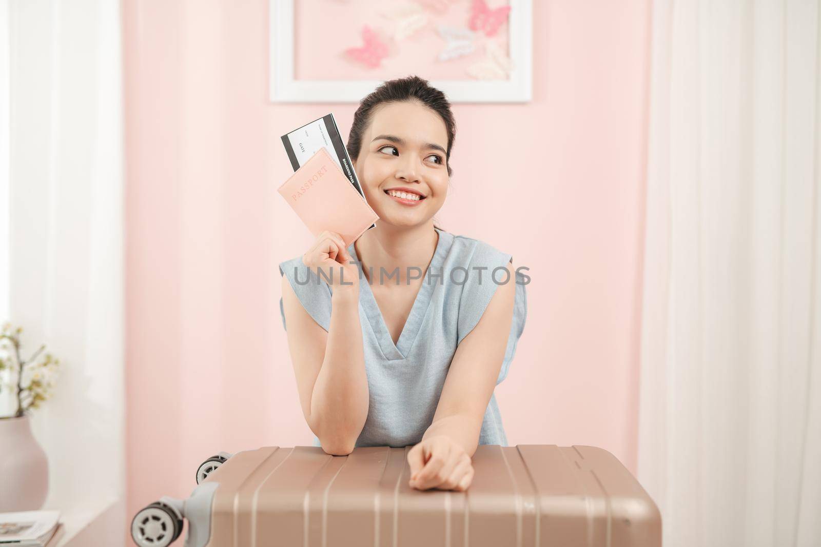 Happy woman is packing suitcase at home with passport and ticket in hand while suitcase is standing nearby by makidotvn