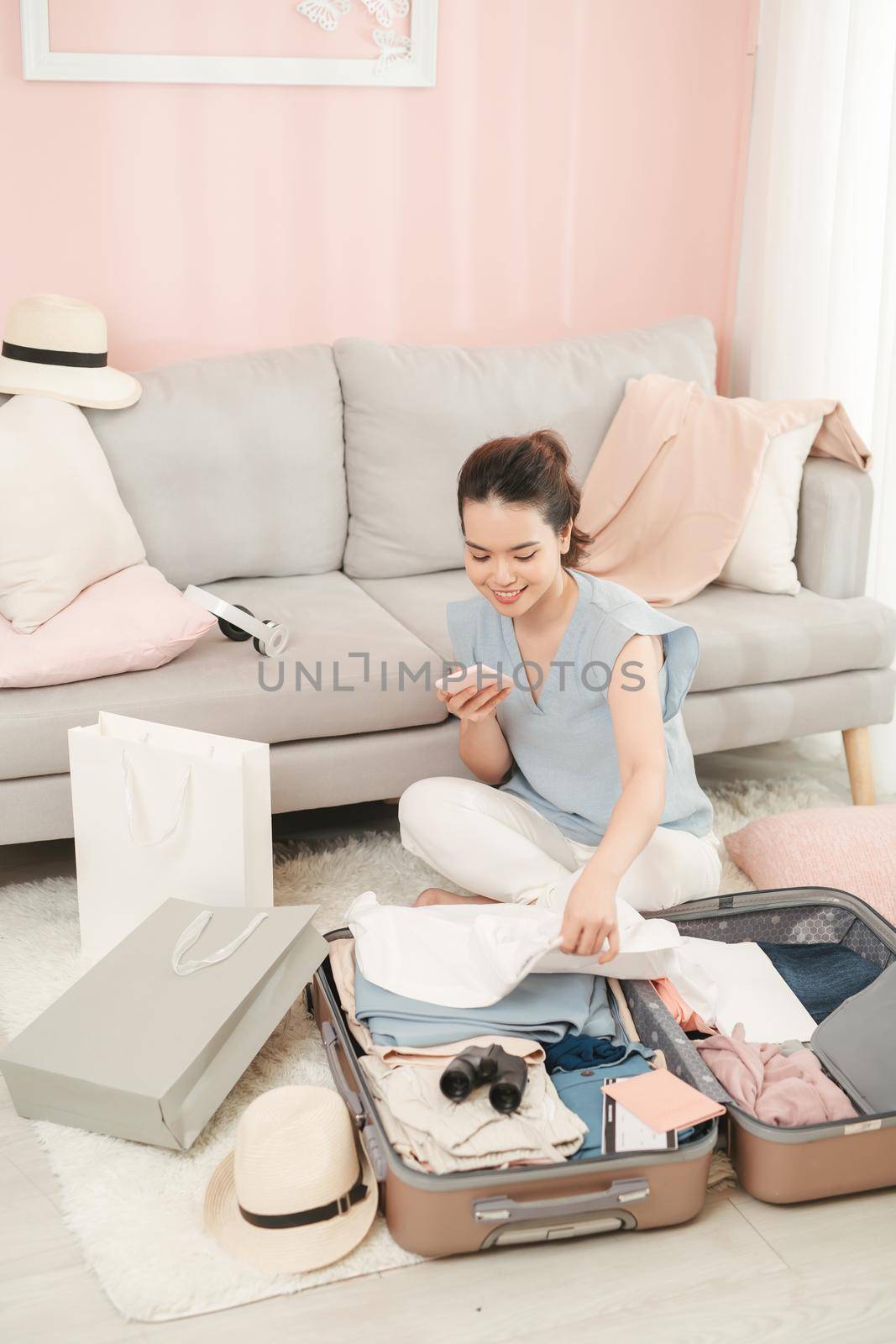 Preparing for holidays. Happy woman texting on phone with suitcase nearby by makidotvn