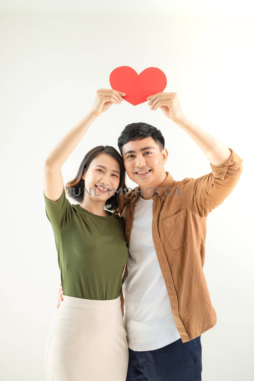Beautiful young loving couple is holding a card in the shape of heart over white background. by makidotvn