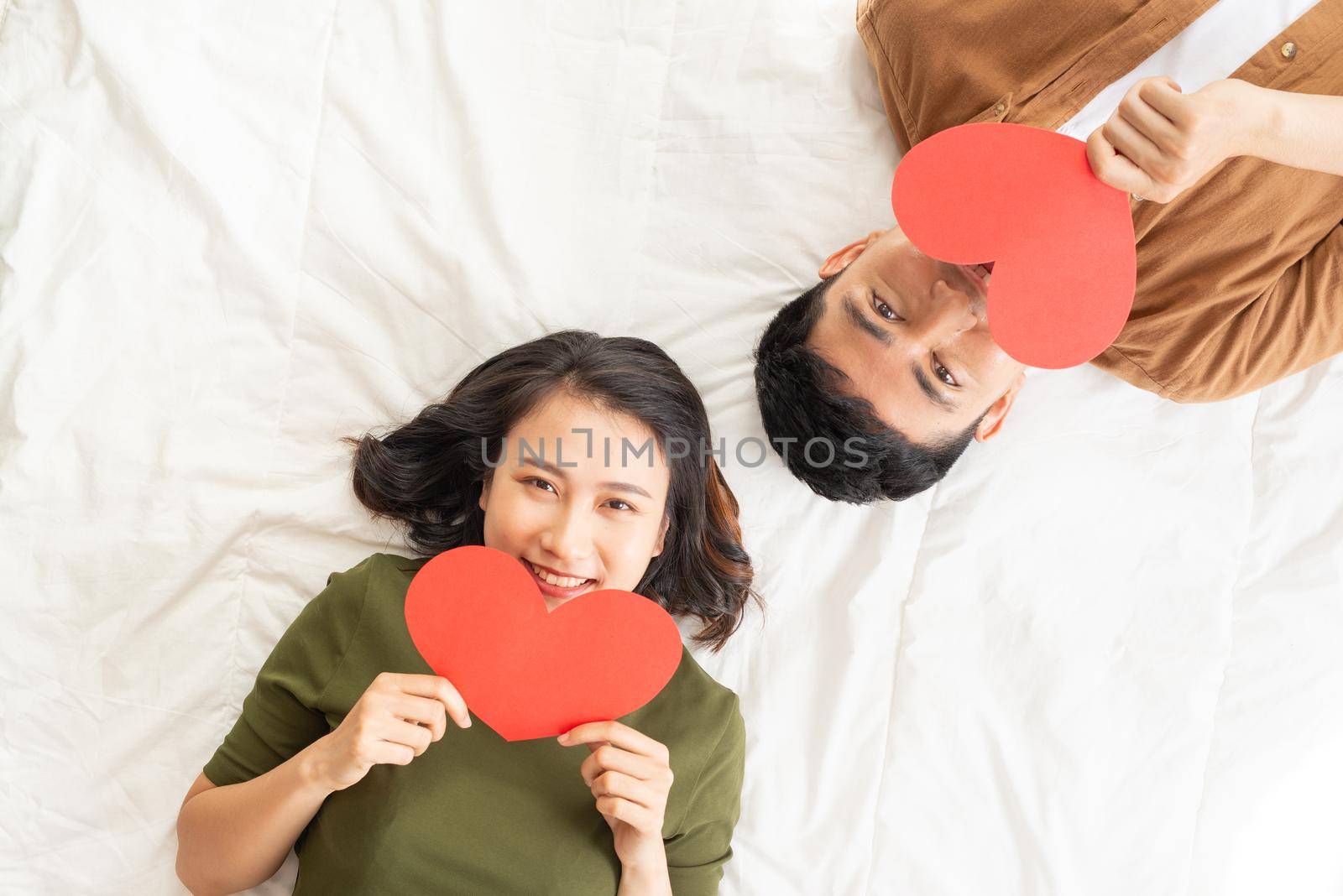 Smiling young couple lying on bed with many heart shapes.