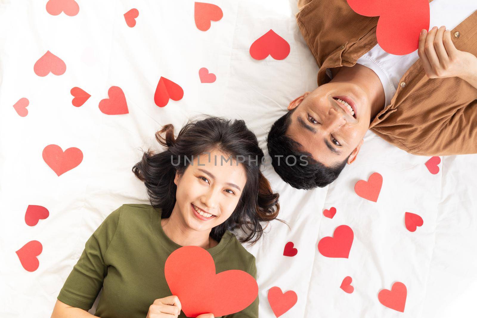 Smiling young couple lying on bed with many heart shapes.