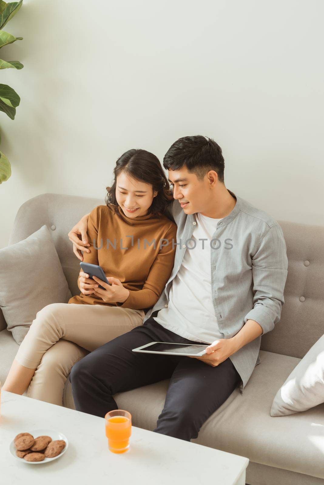 Young couple using a tablet and mobile phone on the couch while enjoying leisure time at home by makidotvn