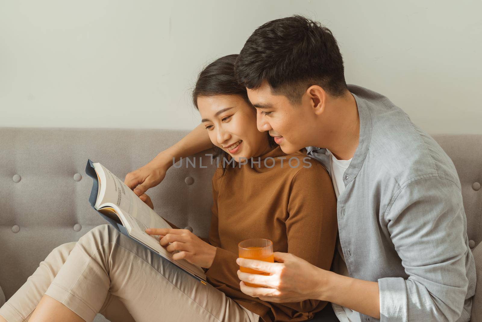 A young, attractive couple is seated together on a couch and are reading a tablet together.