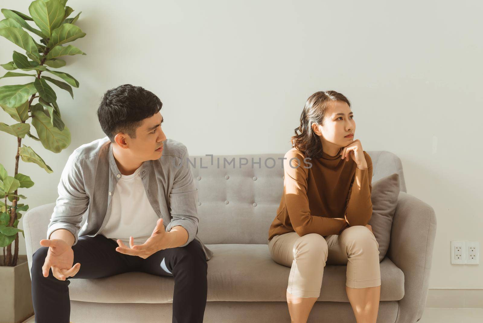 Upset couple at home. Handsome man and beautiful young woman are having quarrel. Sitting on sofa together. Family problems.