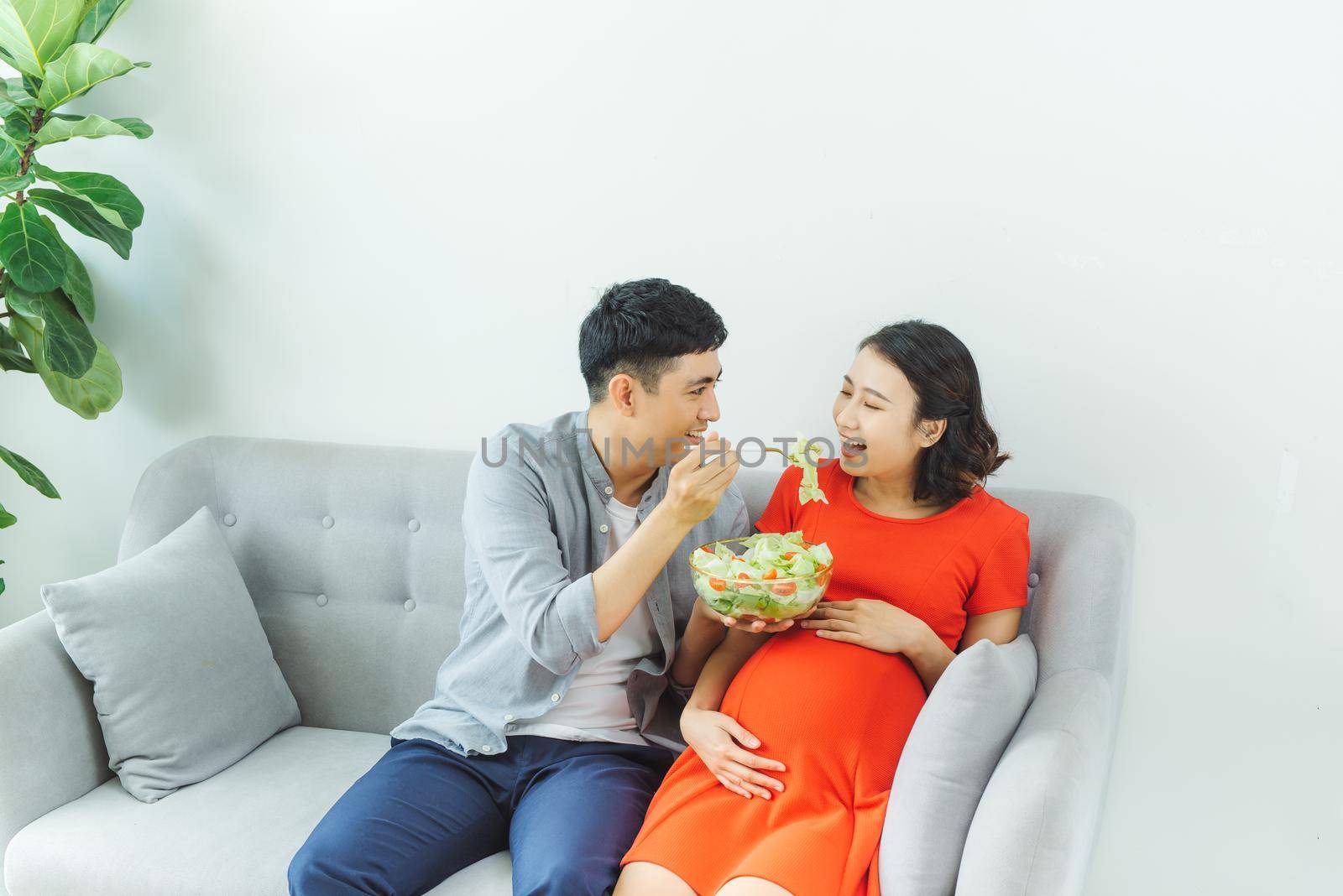 Happy young couple eating salad together at sofa in living room by makidotvn