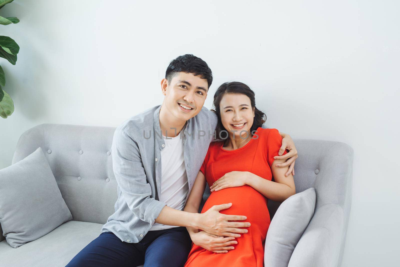 Young couple sitting on couch feeling baby kicking in mother's stomach