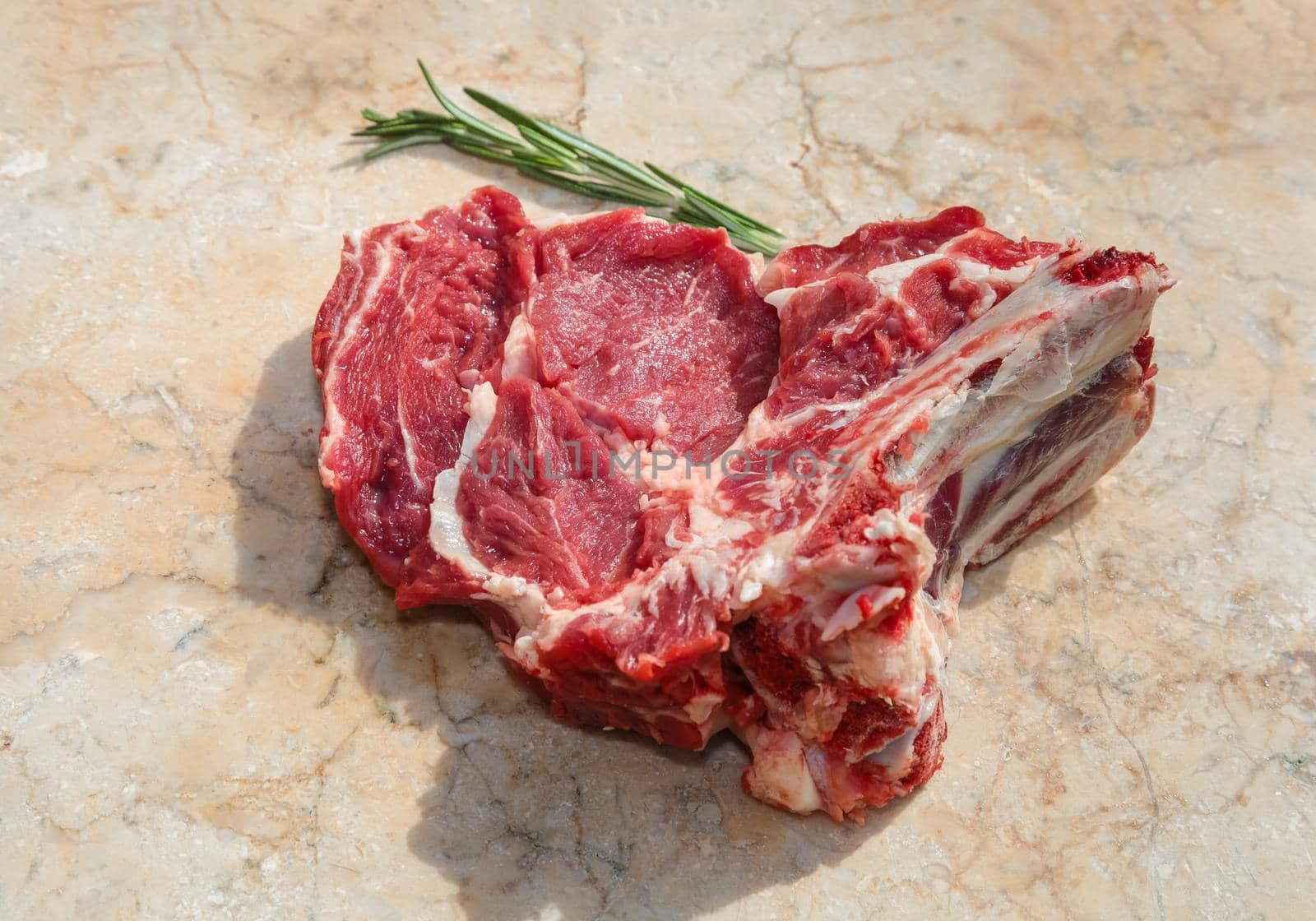 A fresh piece of beef with ribs, ready to roast. Nearby are the spices of rosemary. On a stone cutting board