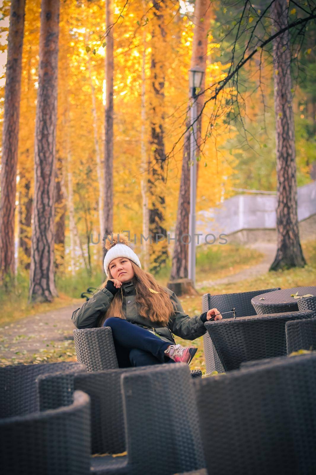 A young girl with long hair sits in a chair in an autumn park.