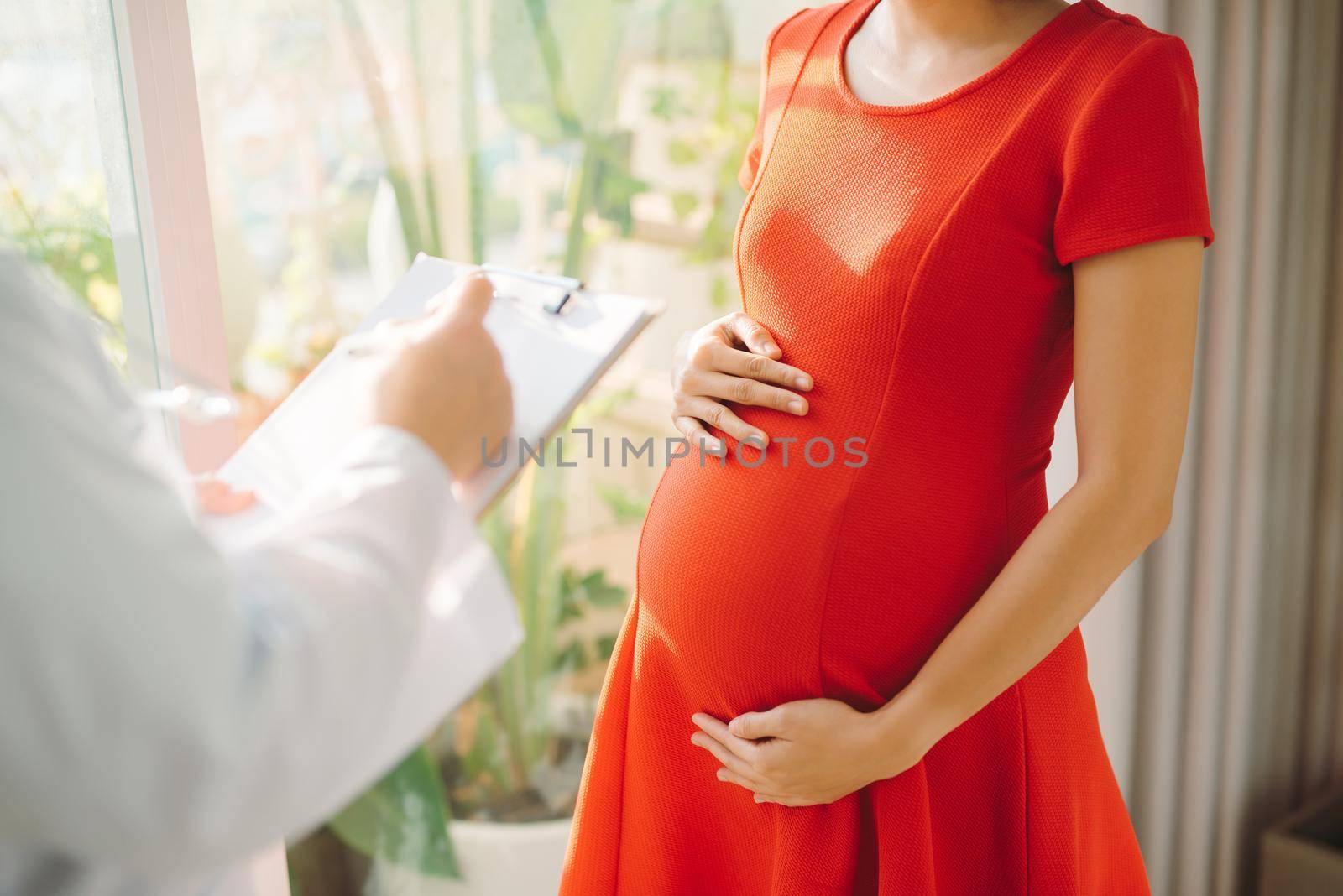 Doctor talking with pregnant woman and giving her explications isolated near window