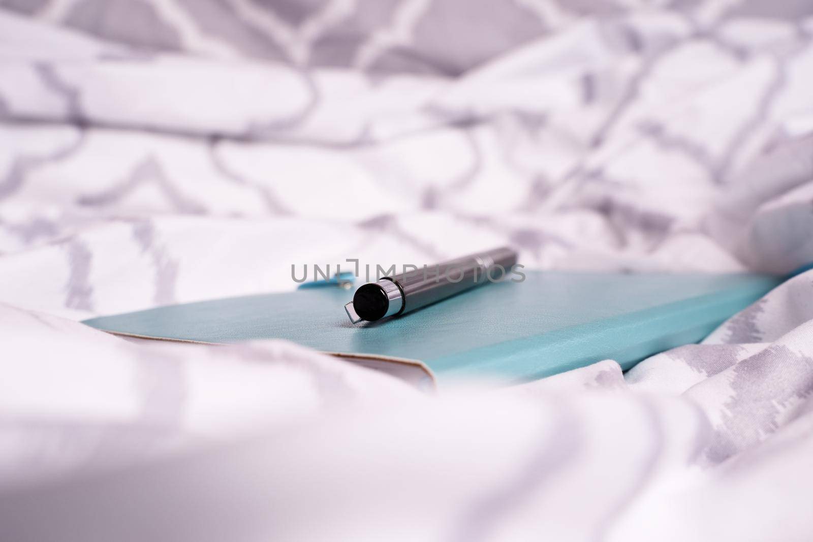 Notepad and pen on bed with modern bright bedsheets by Mendelex