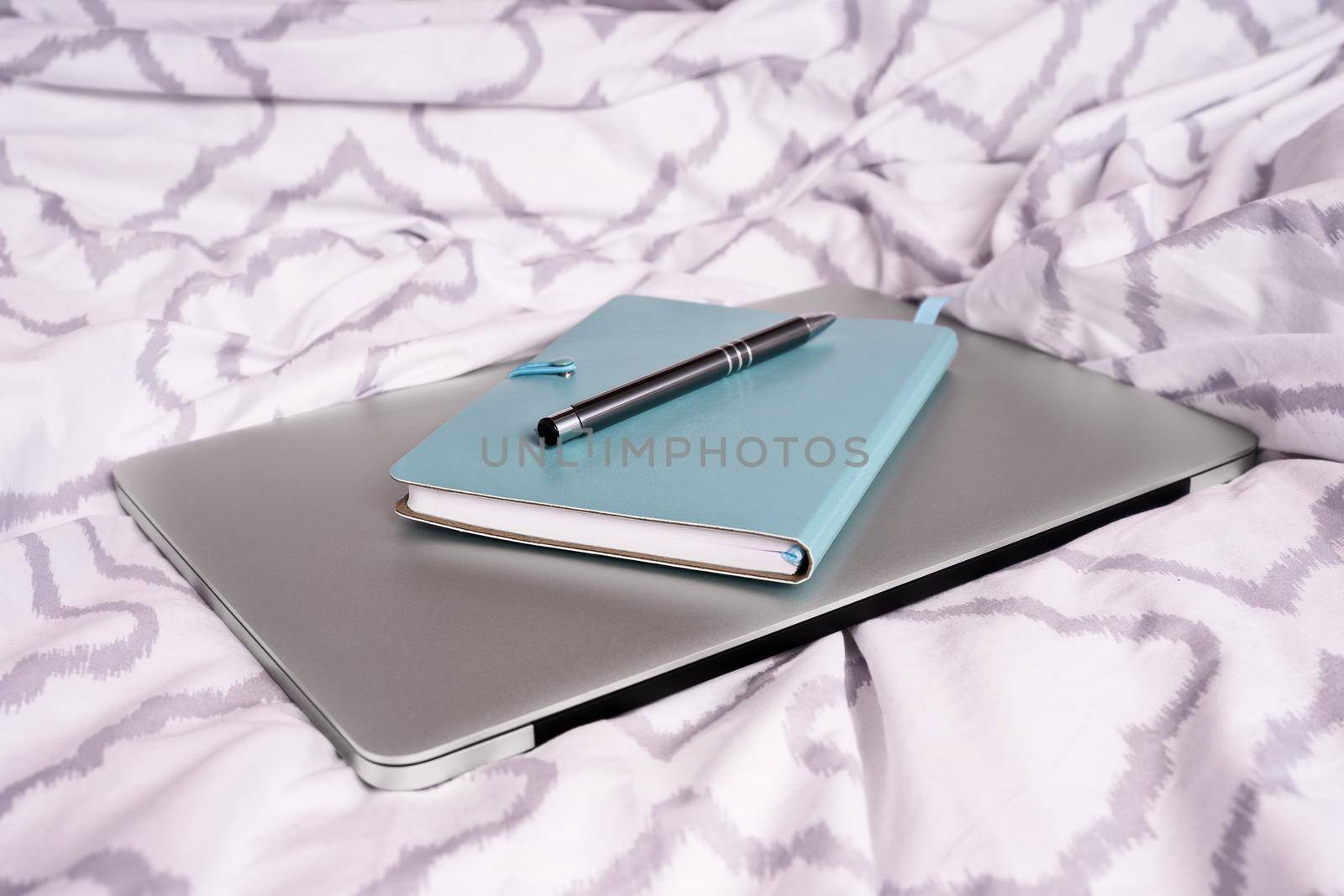 Notepad and pen on top of a laptop computer on bed by Mendelex