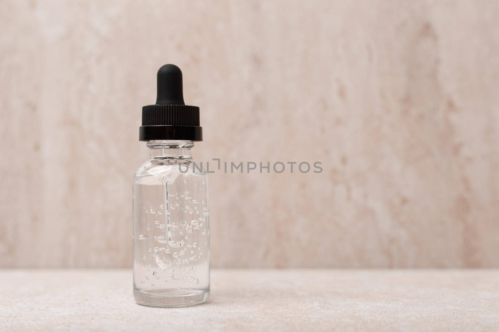 Selective focus, skin serum in transparent bottle with black cap against blurred light marble background with copy space