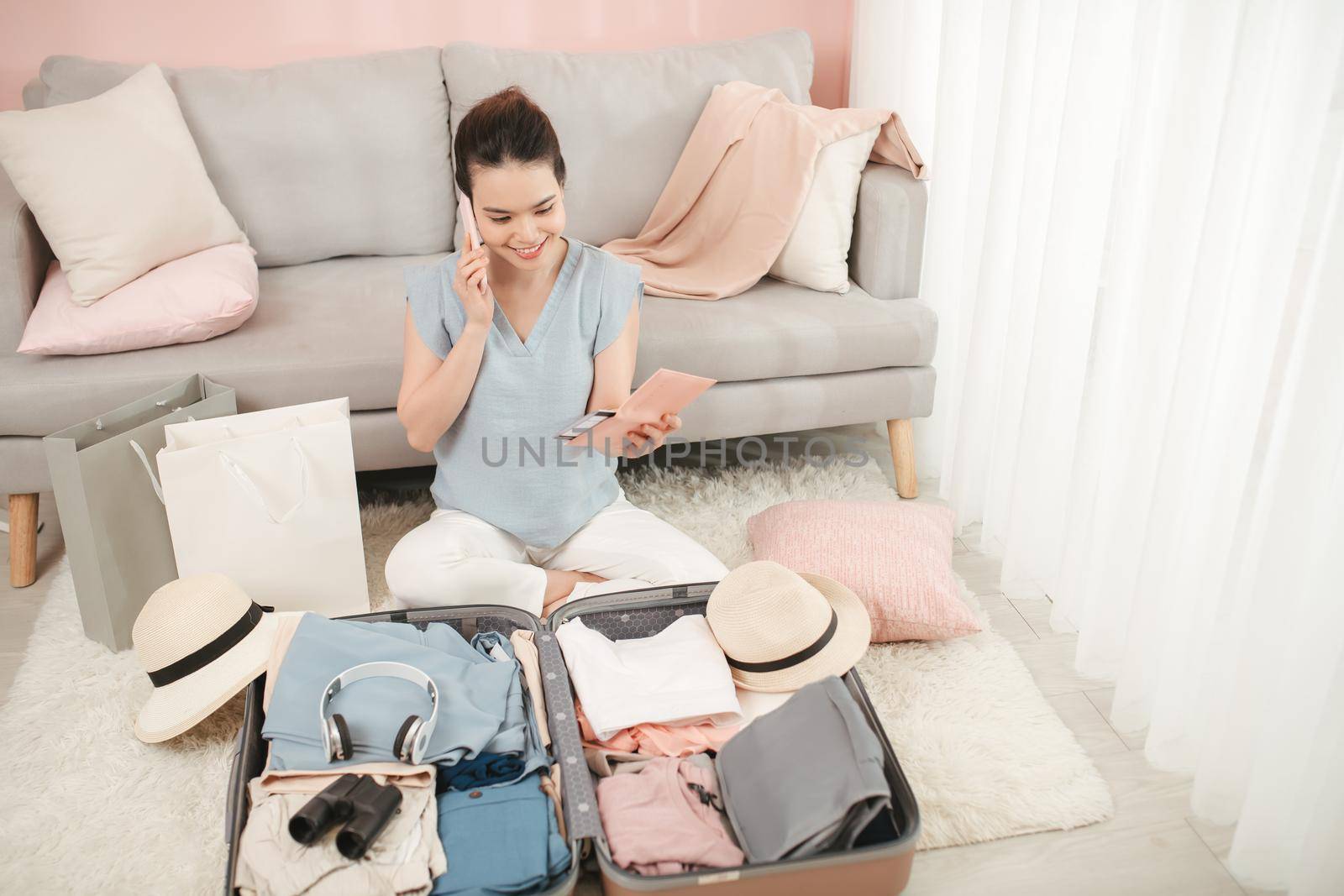 young woman talking with friend on mobile phone holding passport packing travel suitcase in summer holiday trip