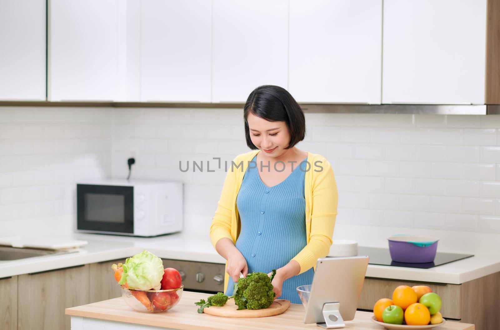 Pregnant woman cutting broccoli for fresh green salad, female prepares tasty organic dinner at home