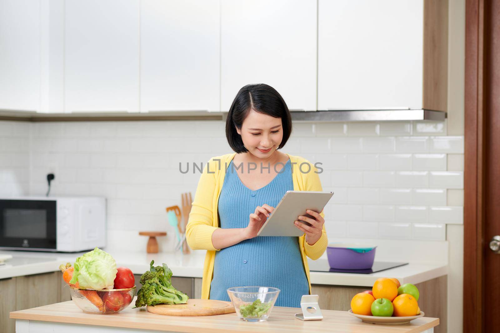 pregnant woman on kitchen making healthy salad with digital tablet