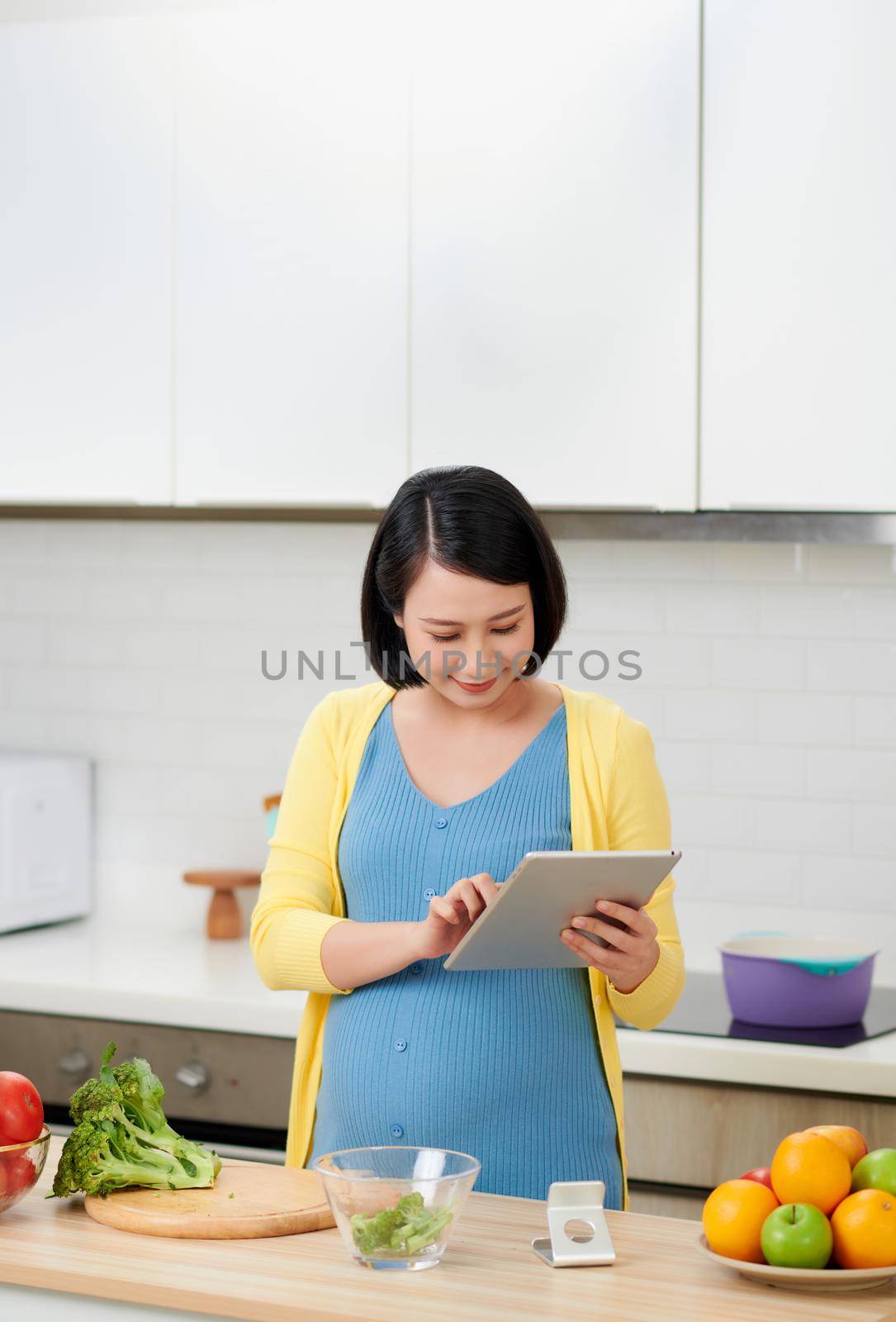 Beautiful pregnant woman using tablet in kitchen