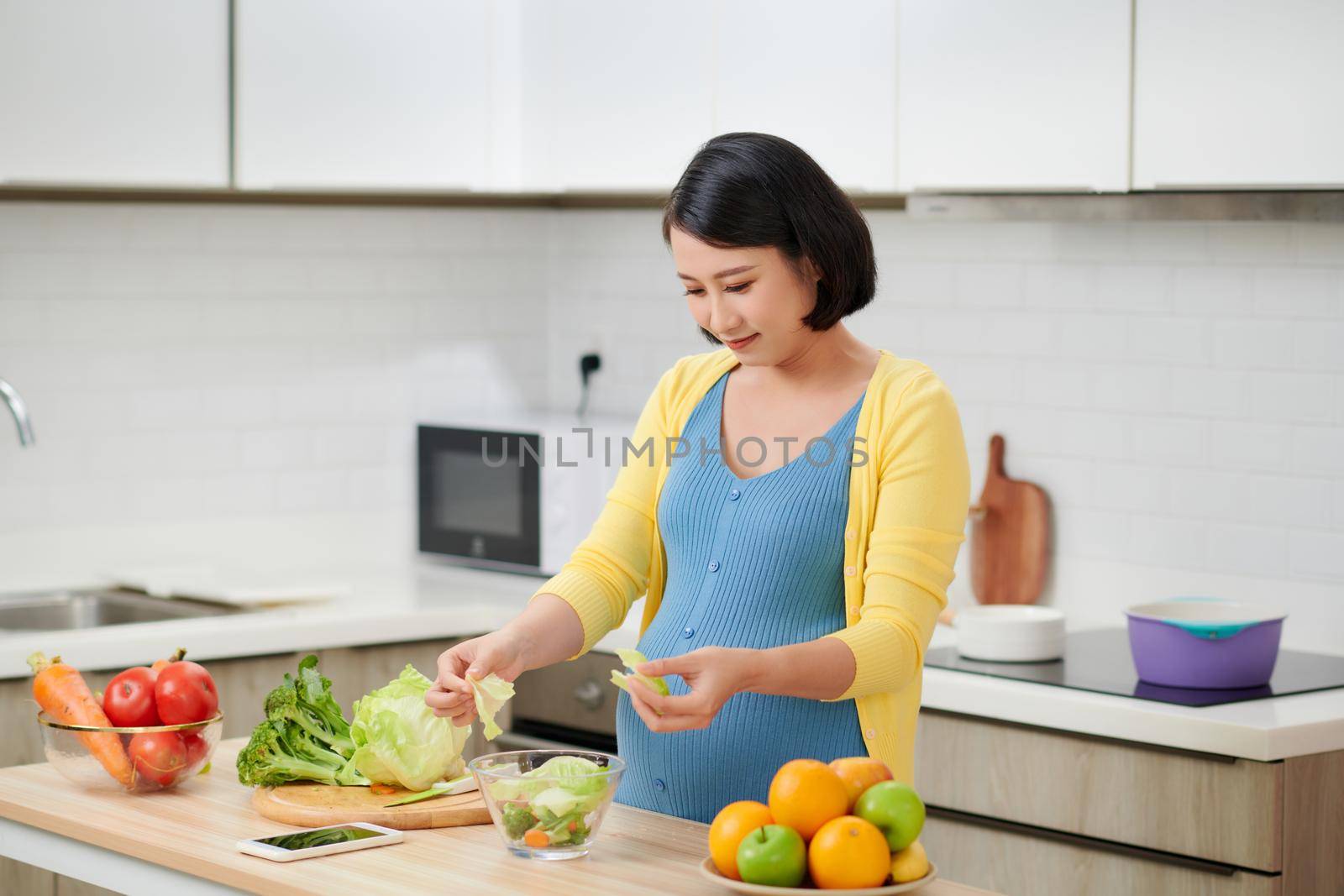 happy pregnant woman on kitchen making healthy salad