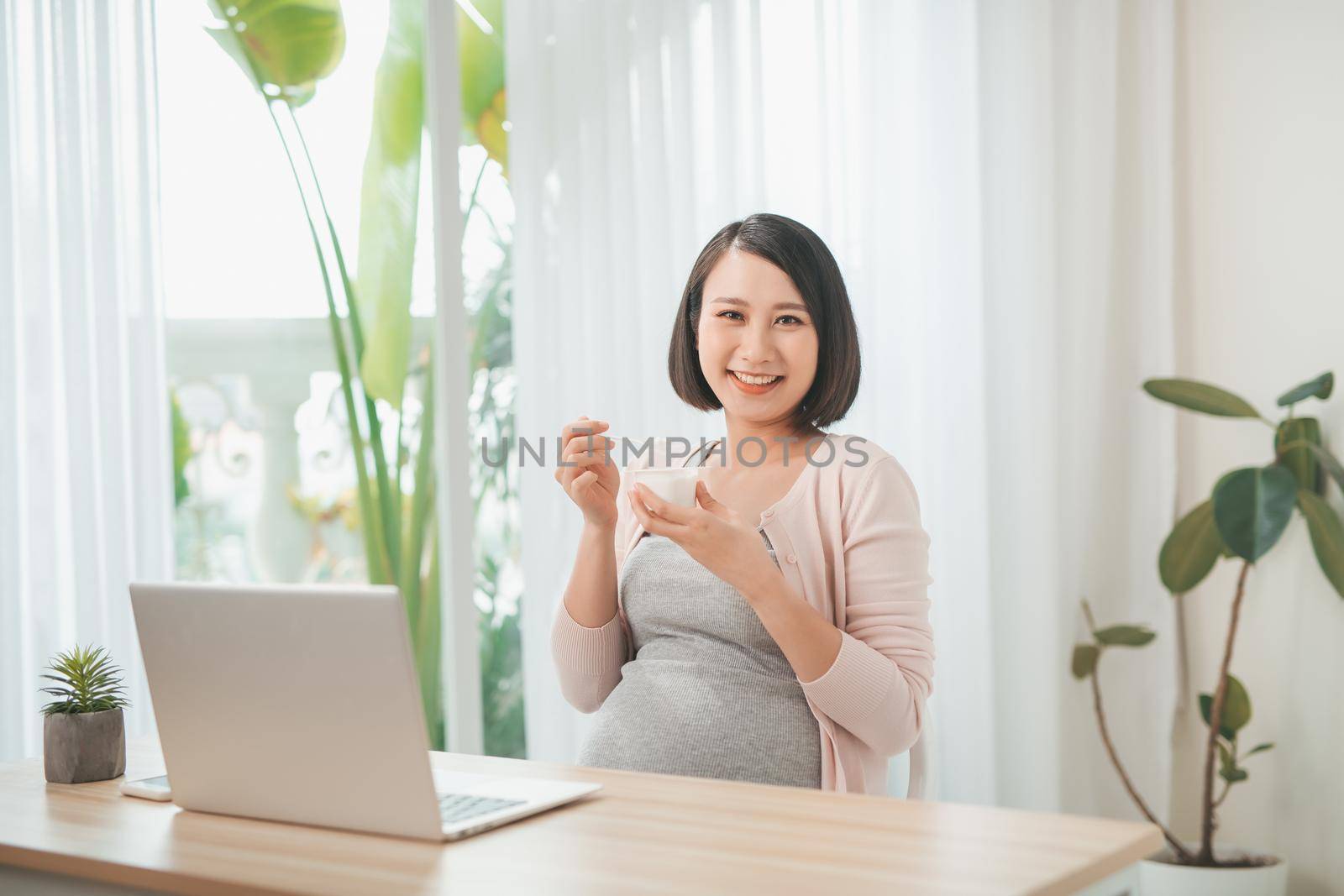 pregnancy, people and rest concept - close up of happy pregnant woman eating yogurt for breakfast at home by makidotvn