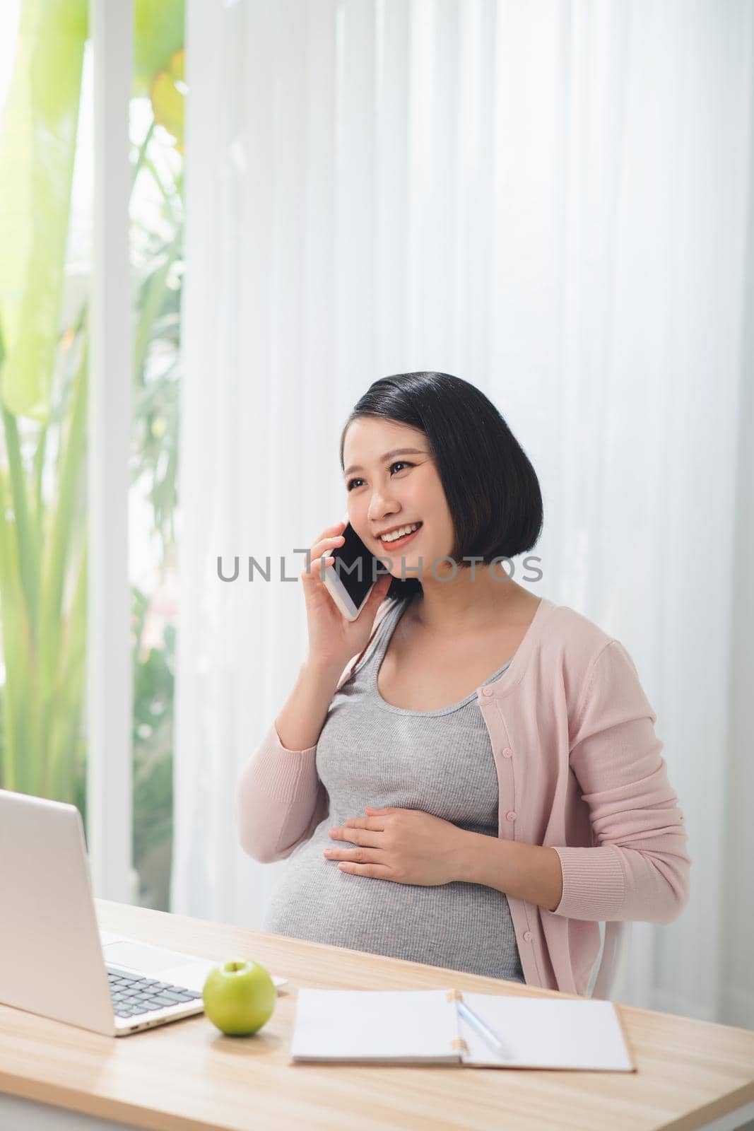 Cheerful asian pregnant woman talking on smart phone