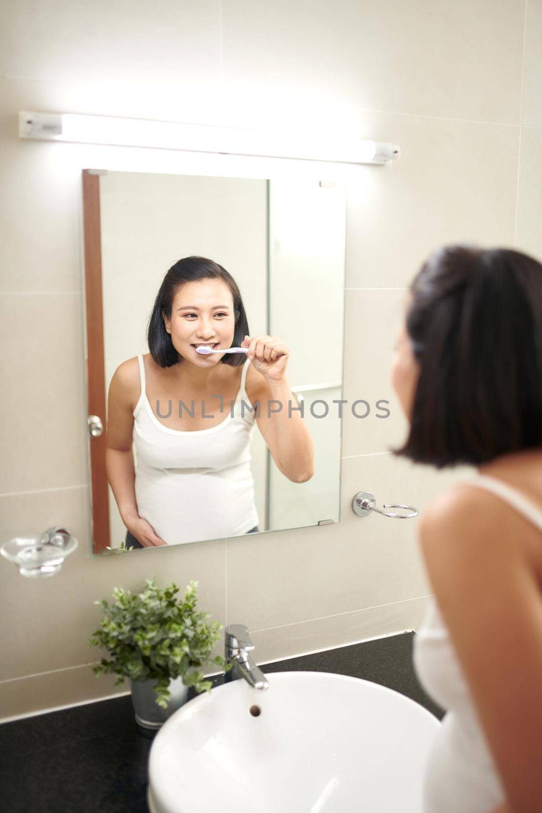 Portrait of beautiful pregnant woman brushing teeth at bathroom by makidotvn