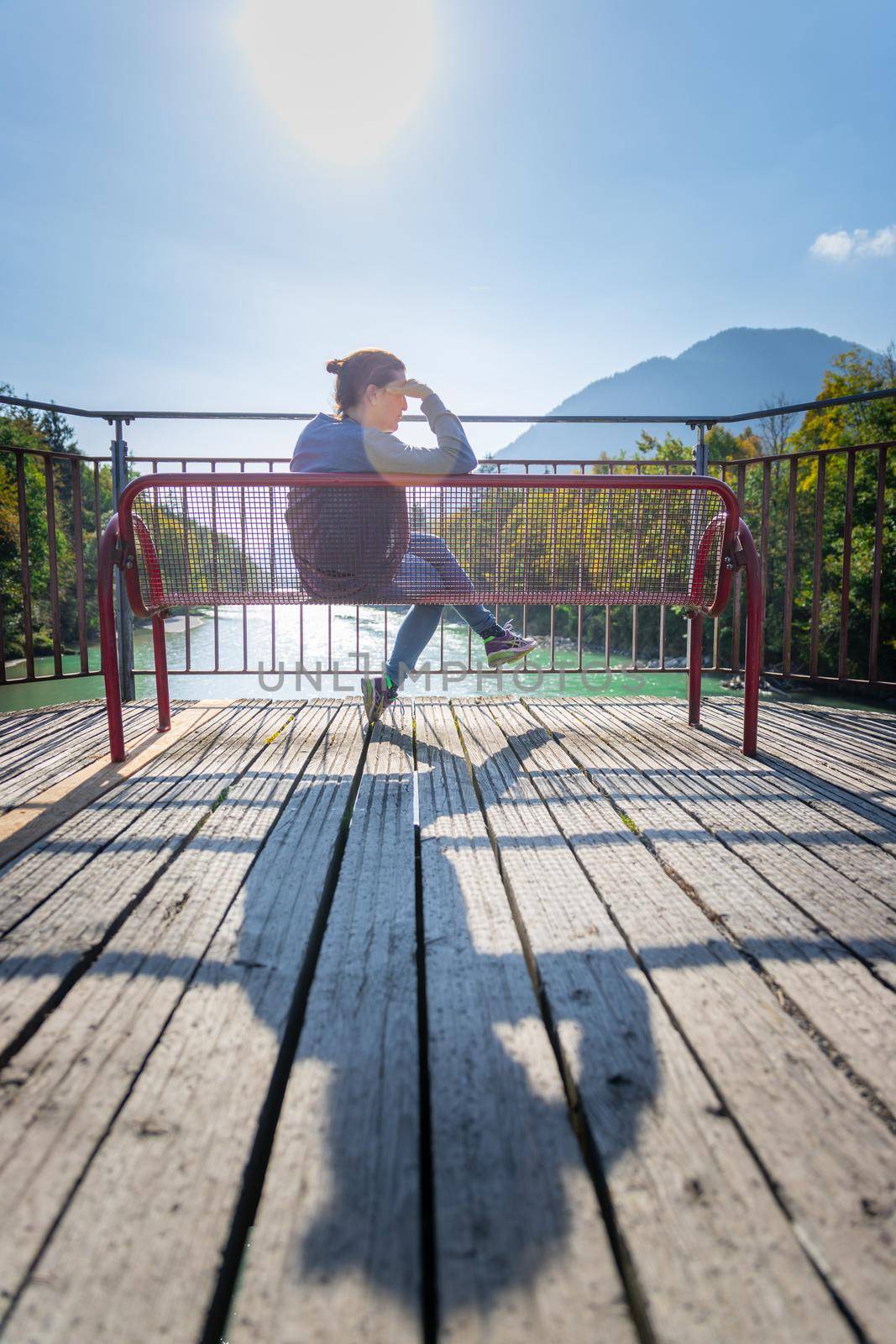 Relaxation concept: Young woman sitting on red bench enjoying the view over a river by Daxenbichler