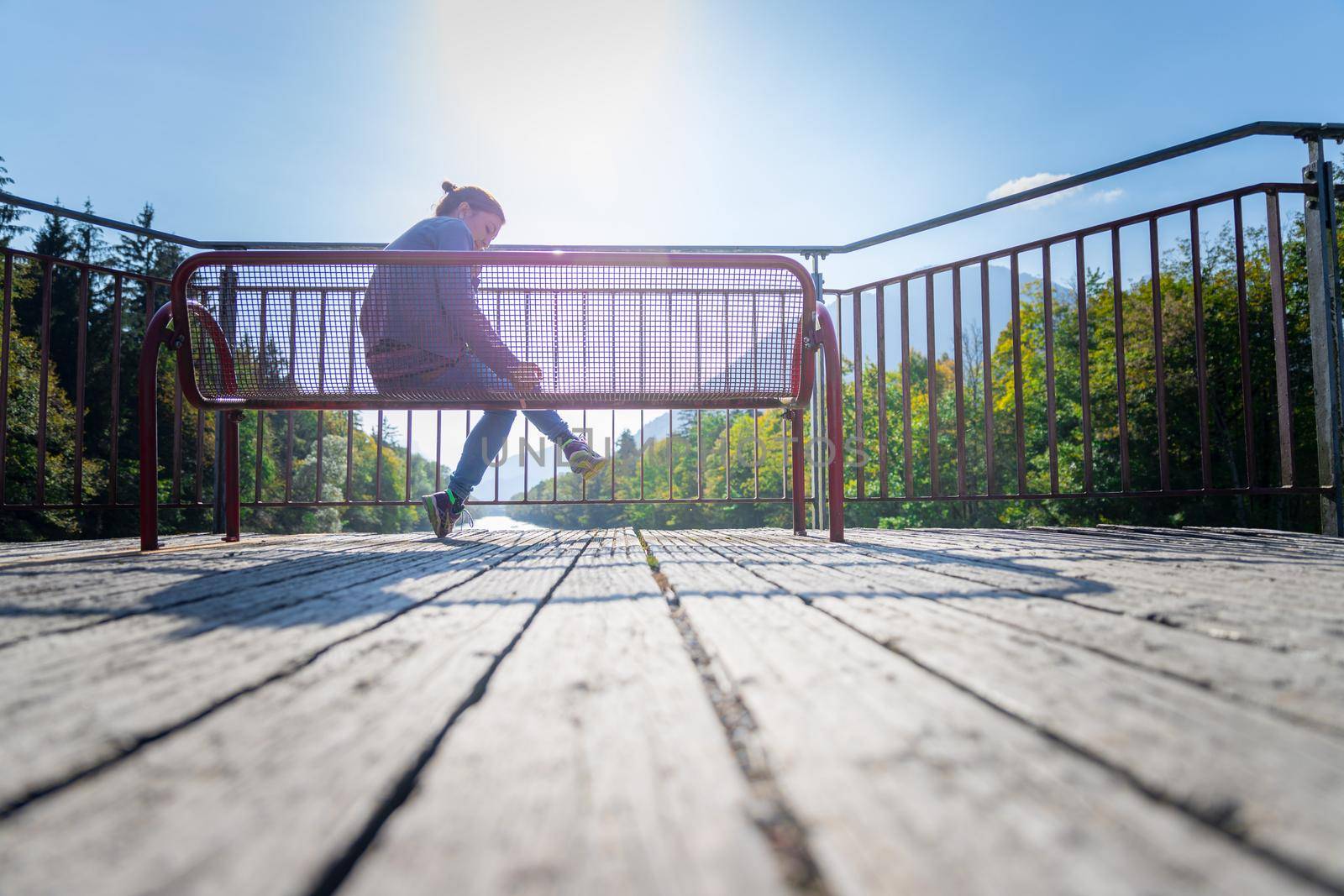 Young woman is sitting on bench, enjoying the view over a river