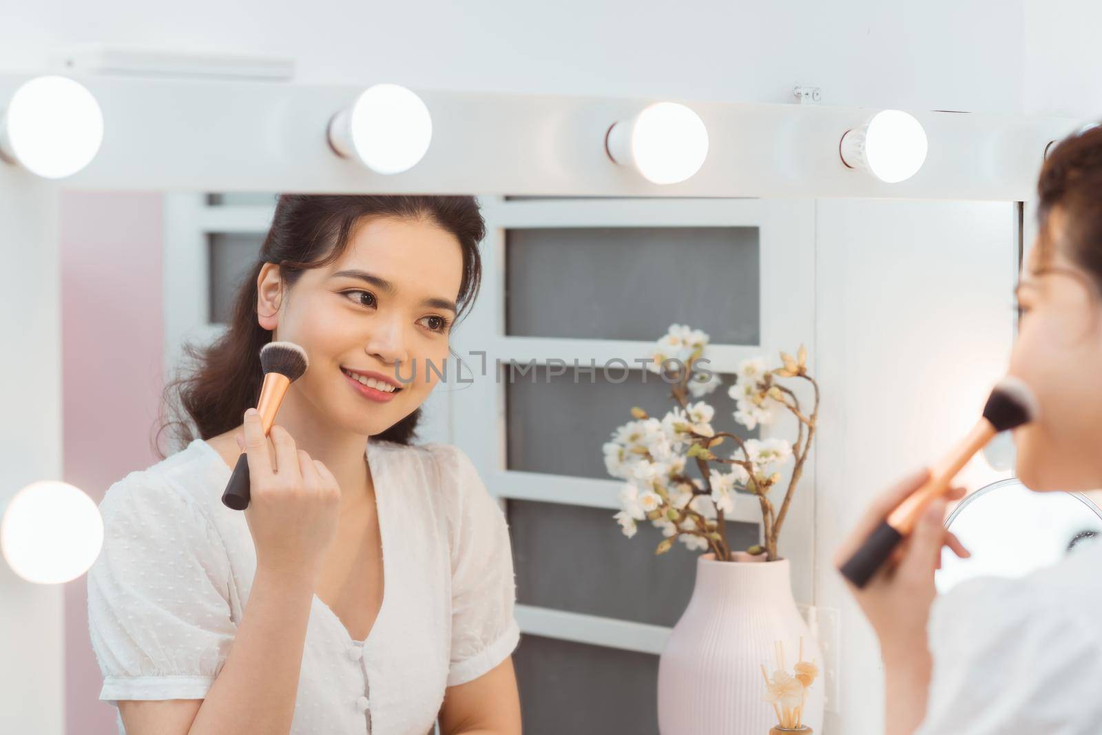 A beautiful young woman sitting at a makeup table and doing her makeup.