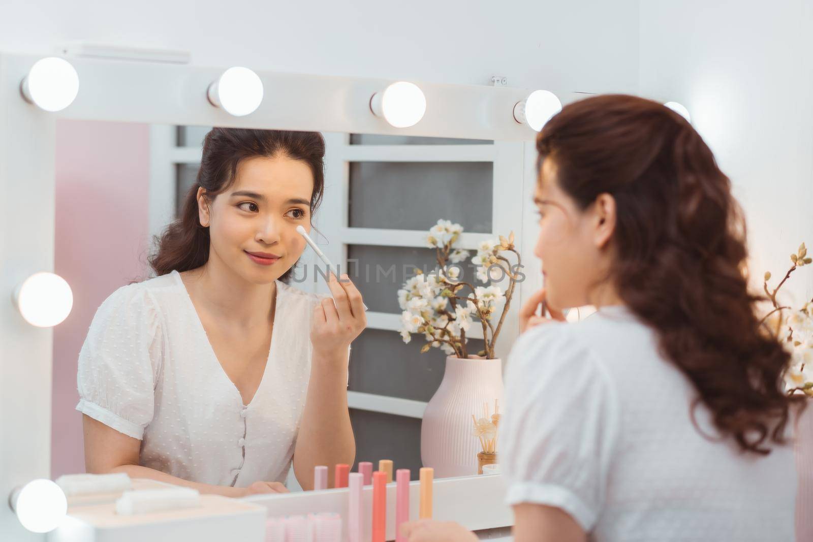 A beautiful young woman sitting at a makeup table and doing her makeup.