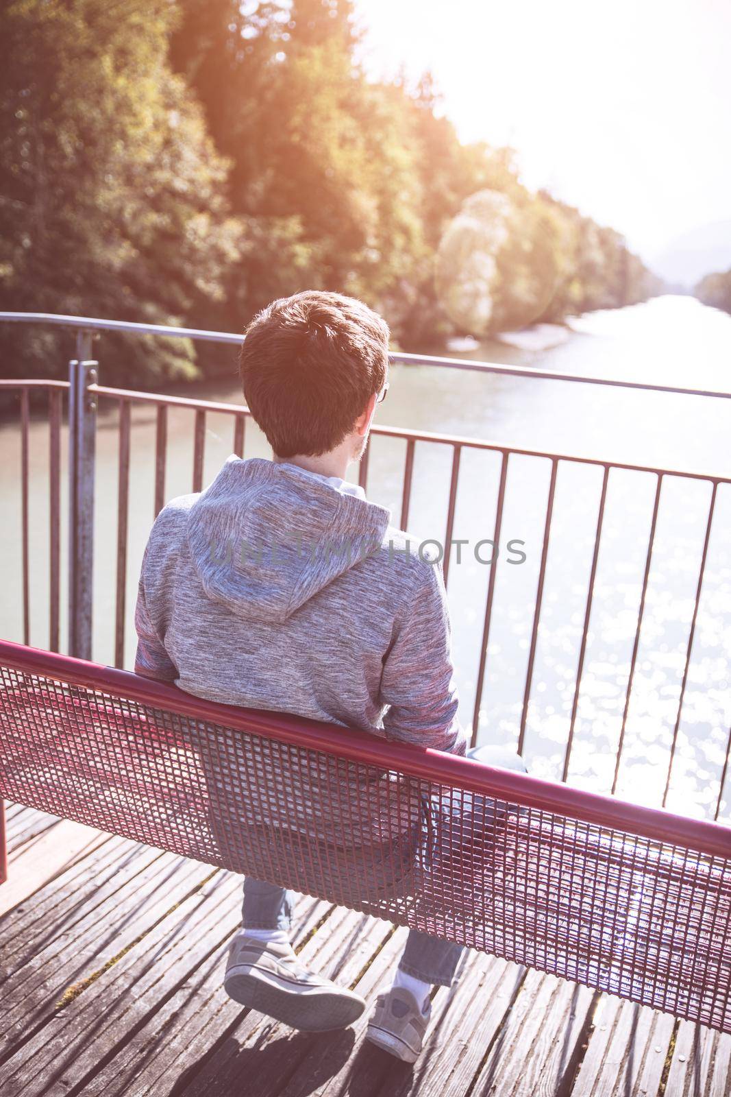 Relaxation concept: Young man sitting on red bench enjoying the view over a river by Daxenbichler
