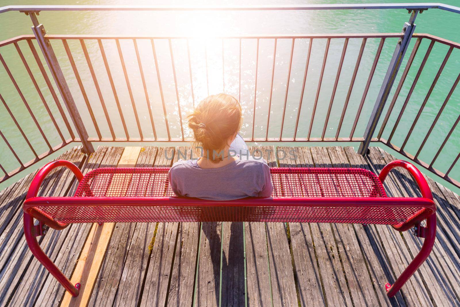 Young woman is sitting on bench, enjoying the view over a river