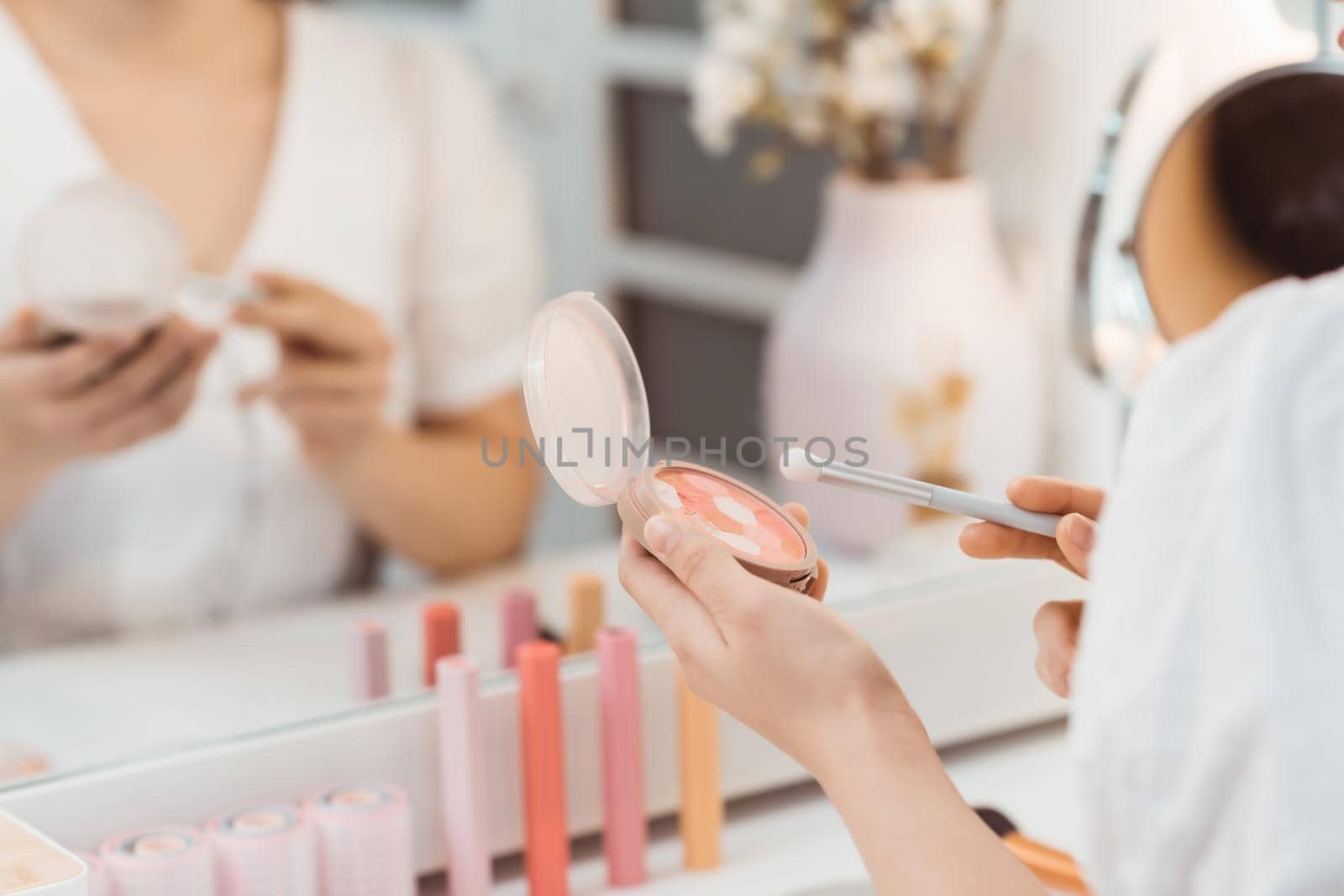 Portrait view of young adult asian woman looking at mirror, sitting in bright room and making make up.