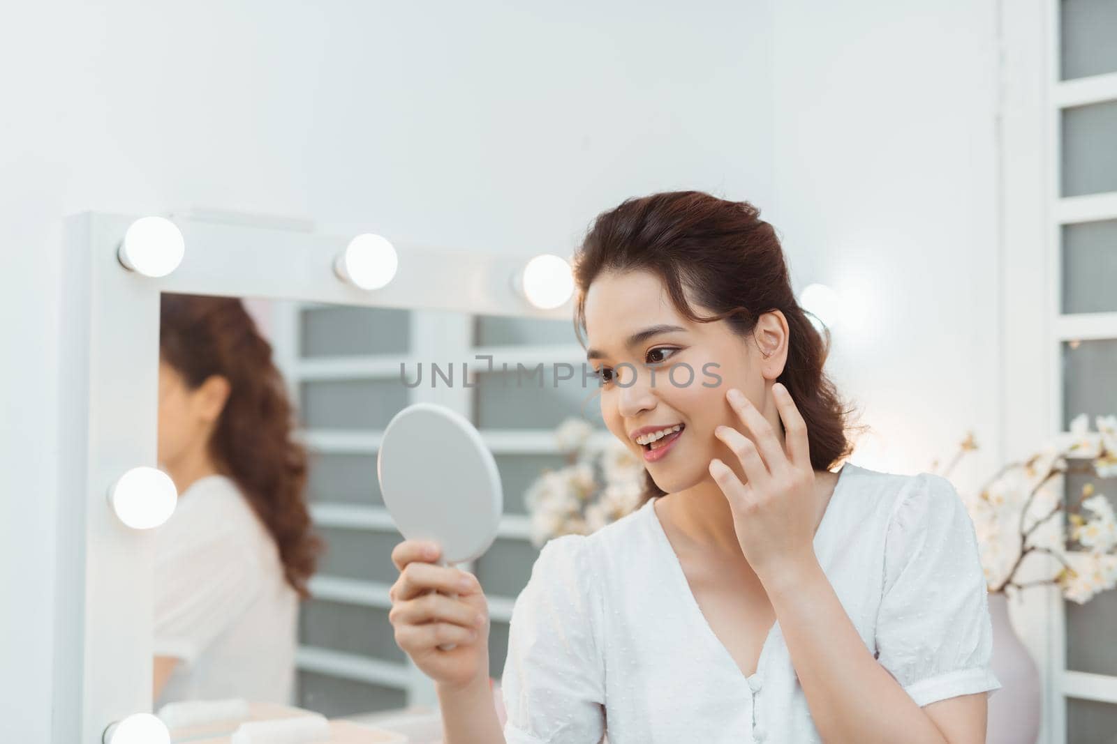 people and beauty concept - beautiful woman with mirror touching her face skin at home bedroom