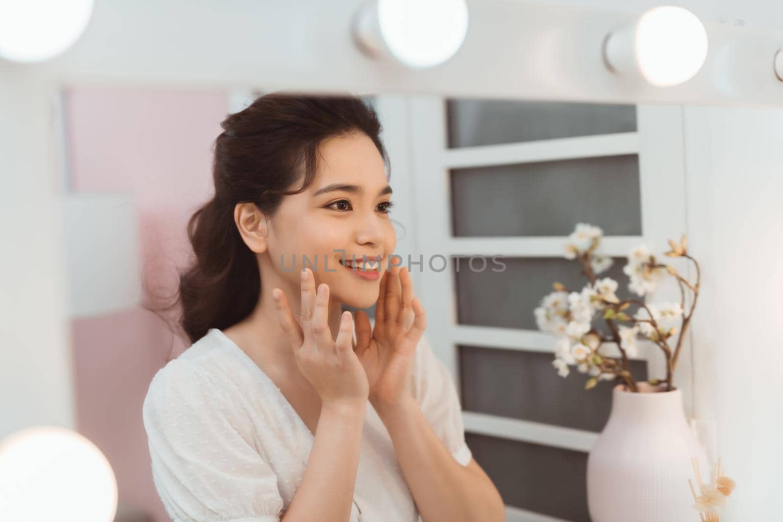 Adult woman checking her face in mirror on light background