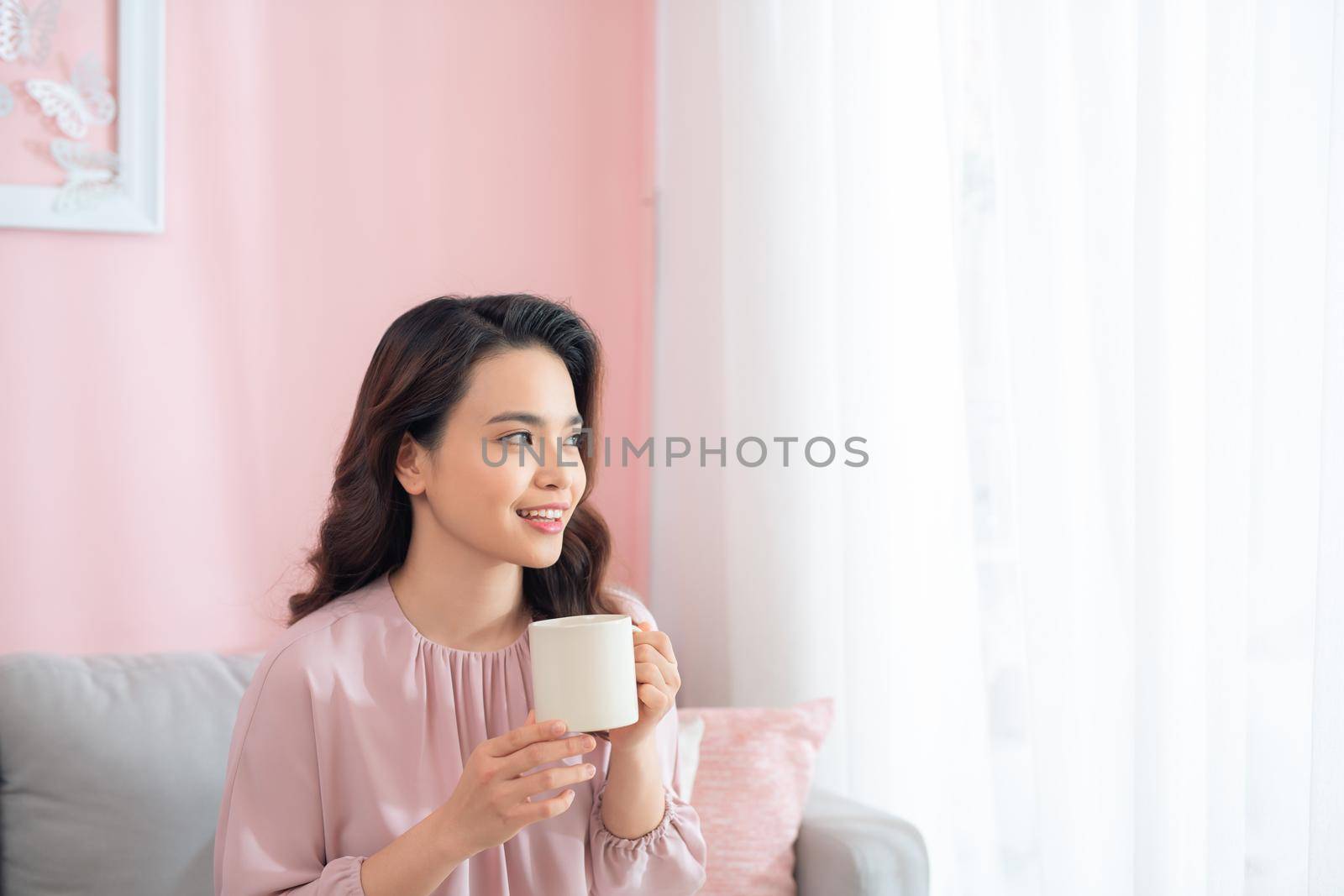 Attractive young Asian woman drinking coffee when sitting on sofa.