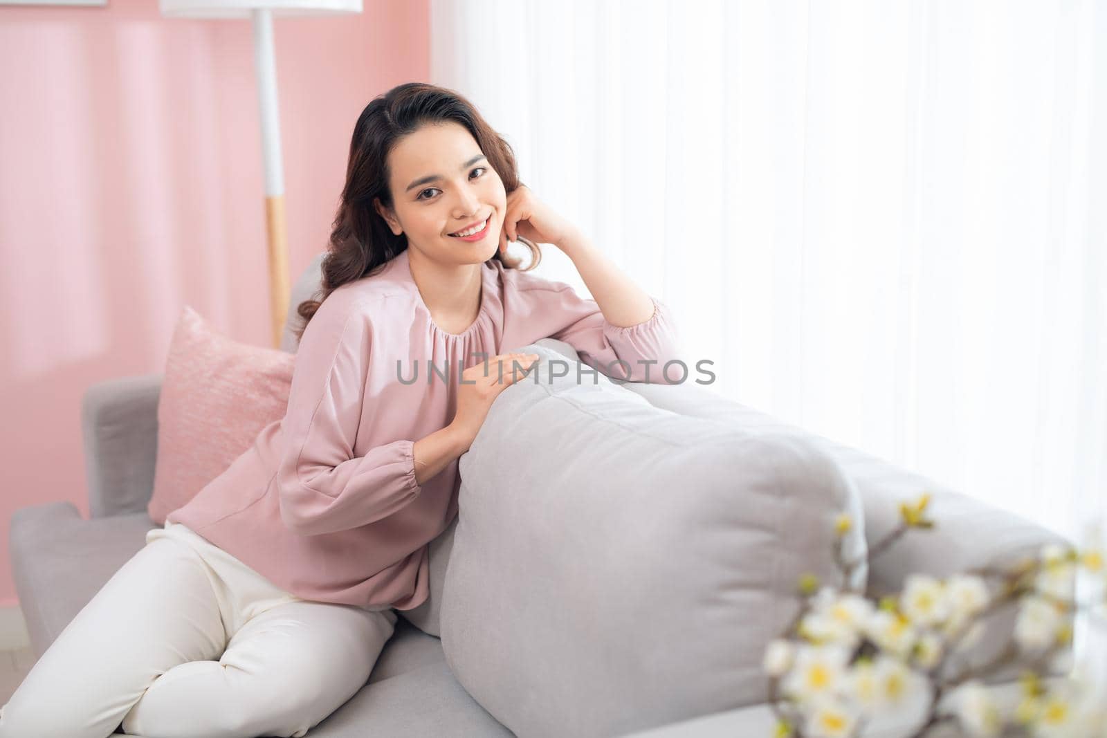 Happy young Asian woman sitting on sofa and relaxing at home.