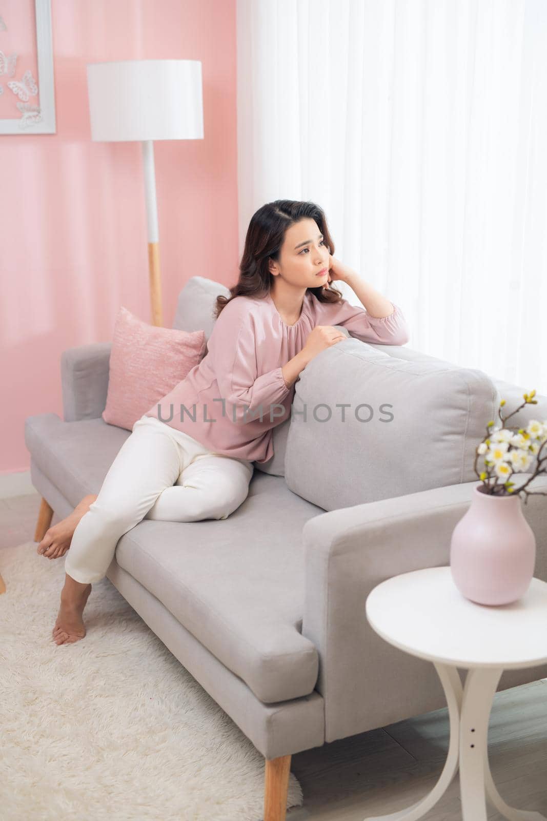 Happy young Asian woman sitting on sofa and relaxing at home.