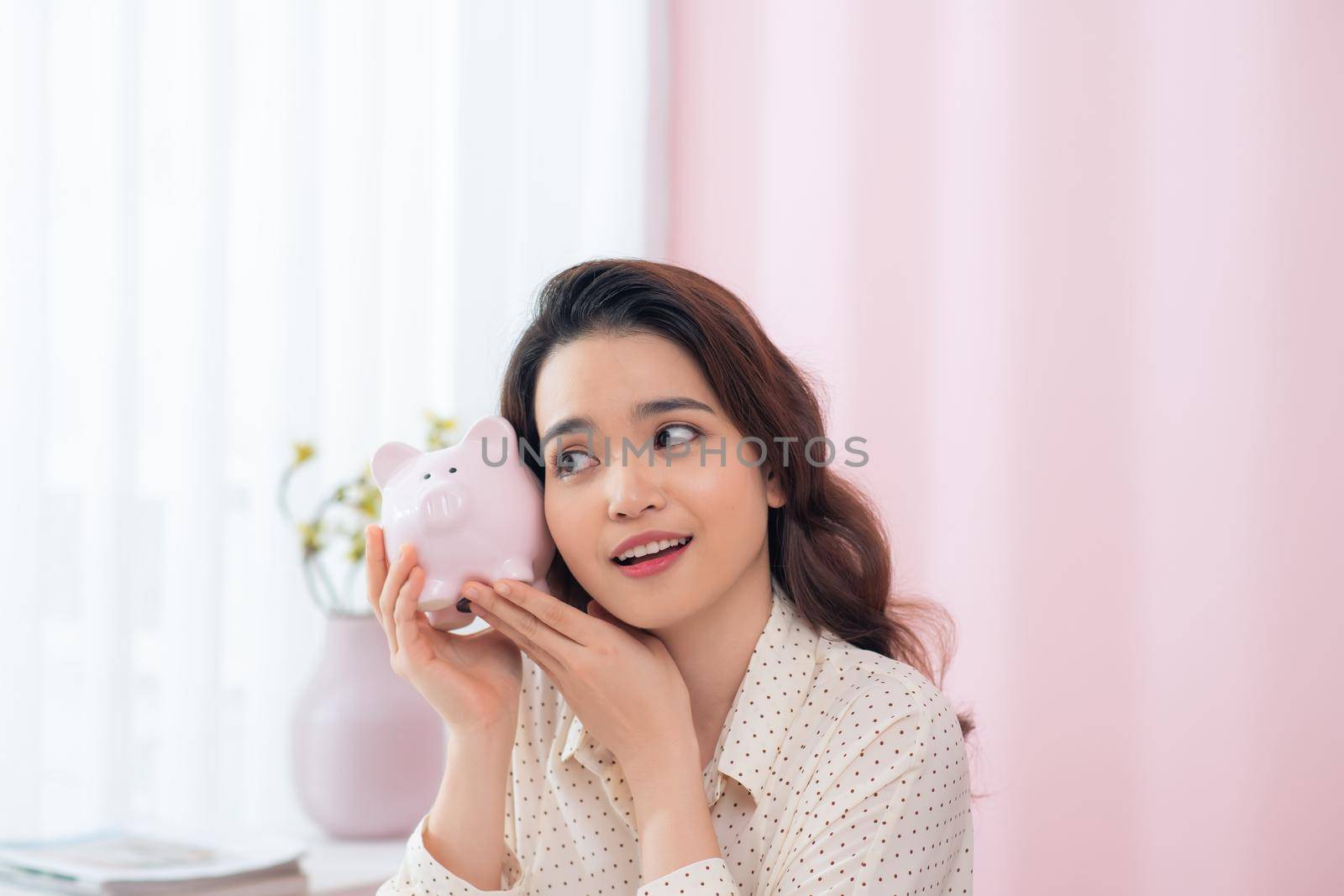 Happy businesswoman holding piggy bank against pink background