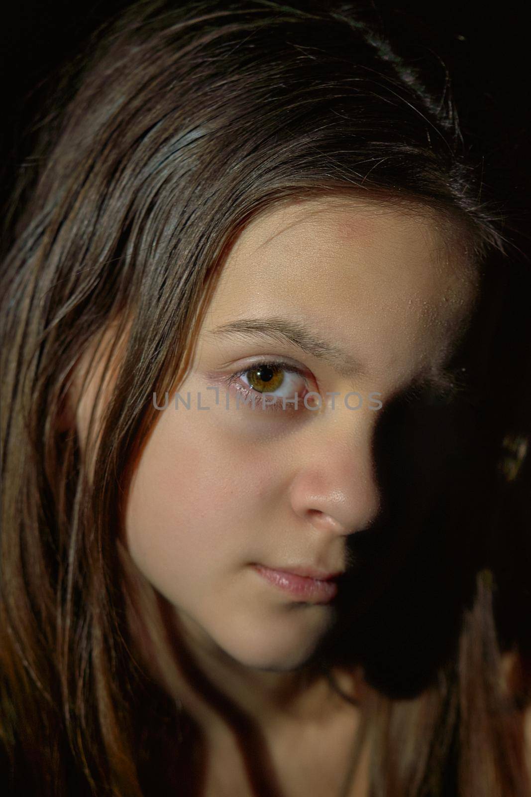 Facial portrait of cute teenage girl with long hair. Vertical shot, dark background