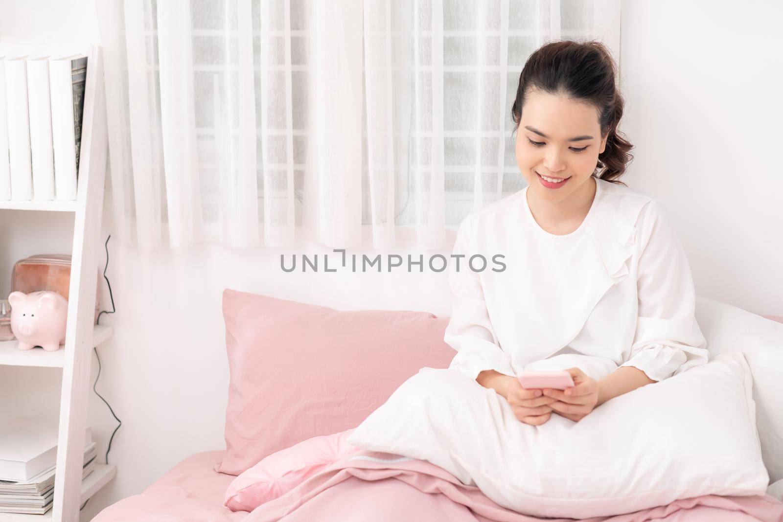 Young asian woman using smart mobile phone in bedroom interior