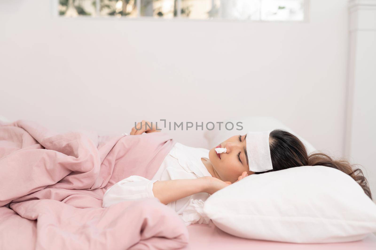 Portrait of a beautiful young woman lying in bed, having a cold and sneezing in a tissue.