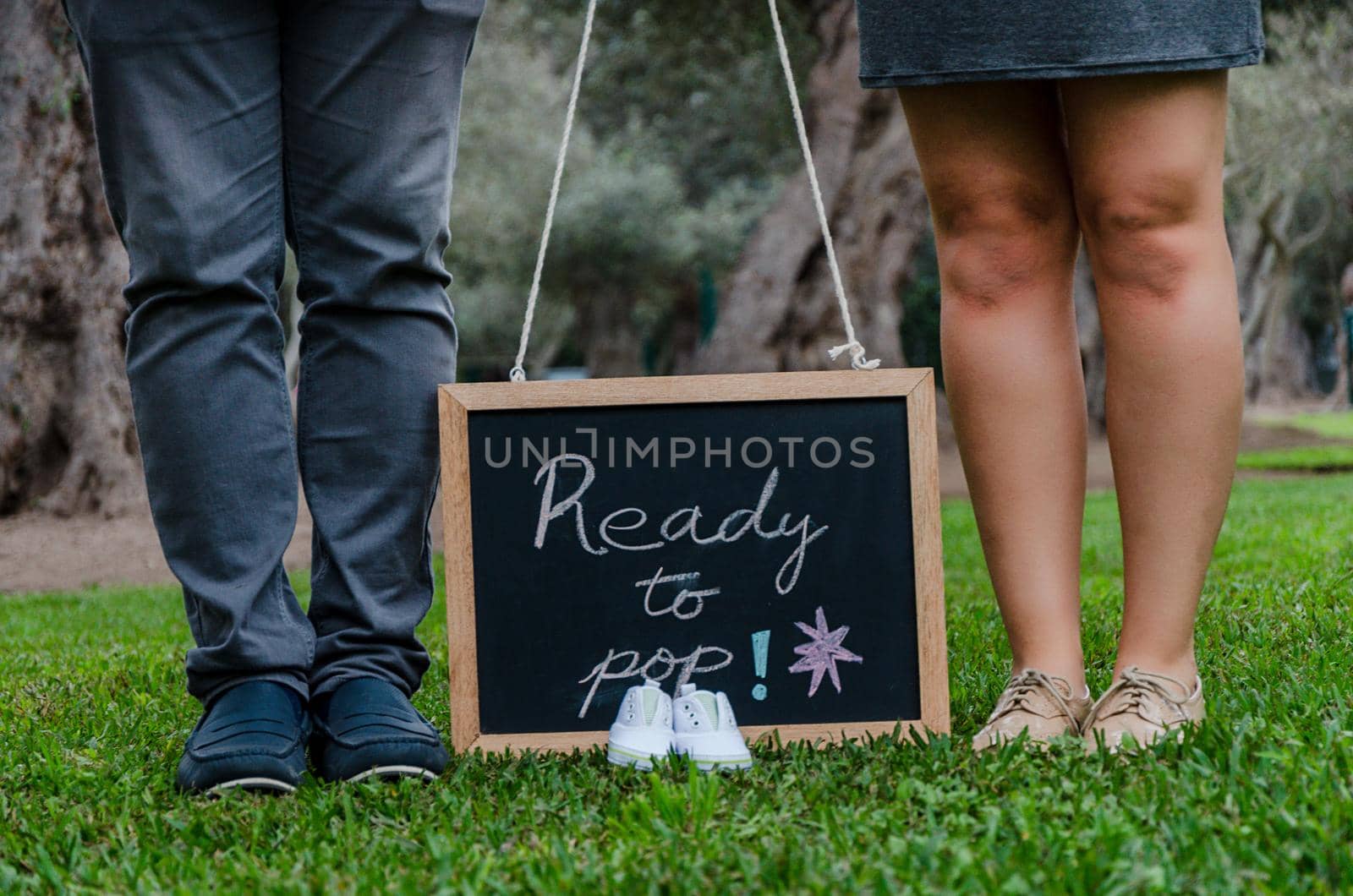 Feet of father and mother with baby shoes and a black slate, concept for the baby's welcome
