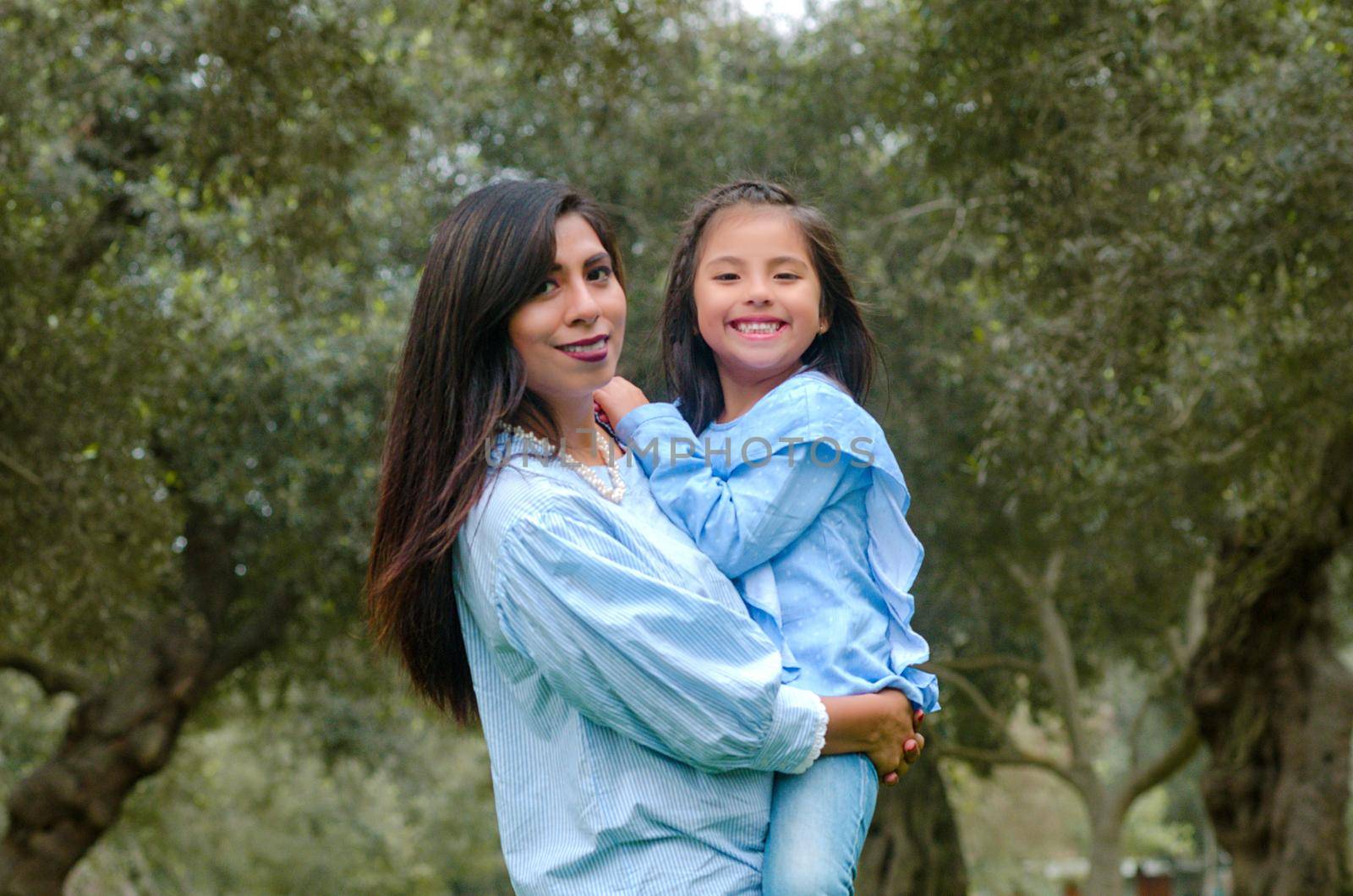 Mother carrying her cute and smiling daughter in the park on a winter afternoon