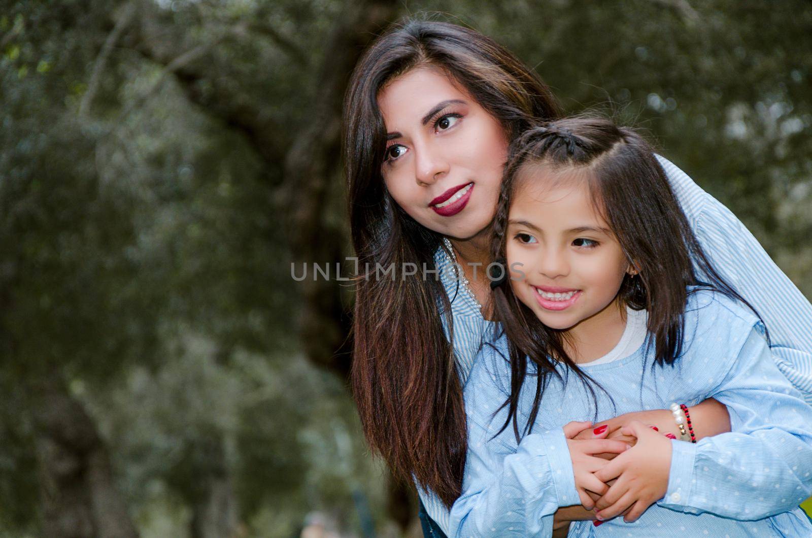 Mother carrying her cute and smiling daughter in the park on a winter afternoon