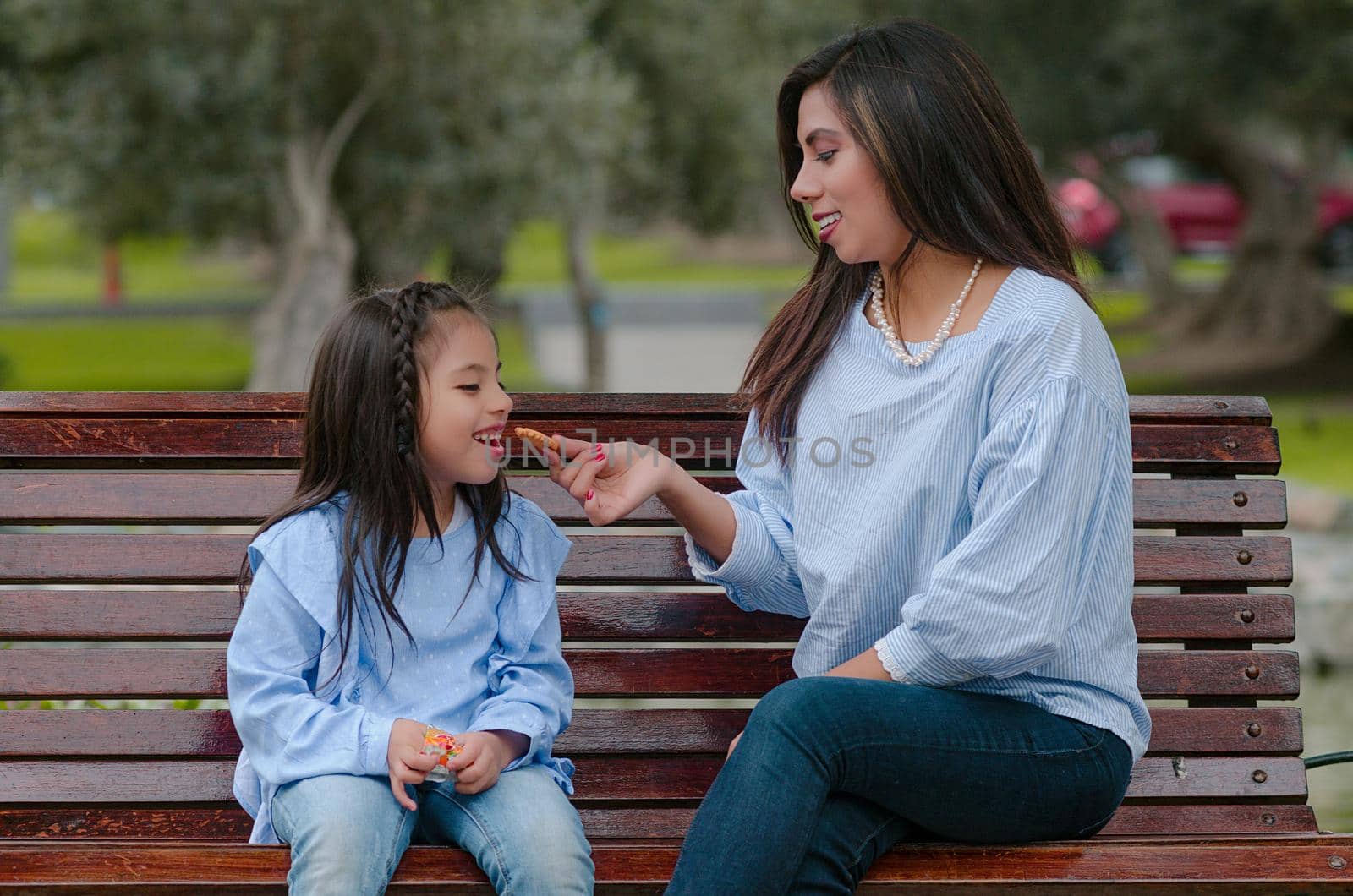 Mother and her little daughter sitting on a bench eating a cookie by Peruphotoart