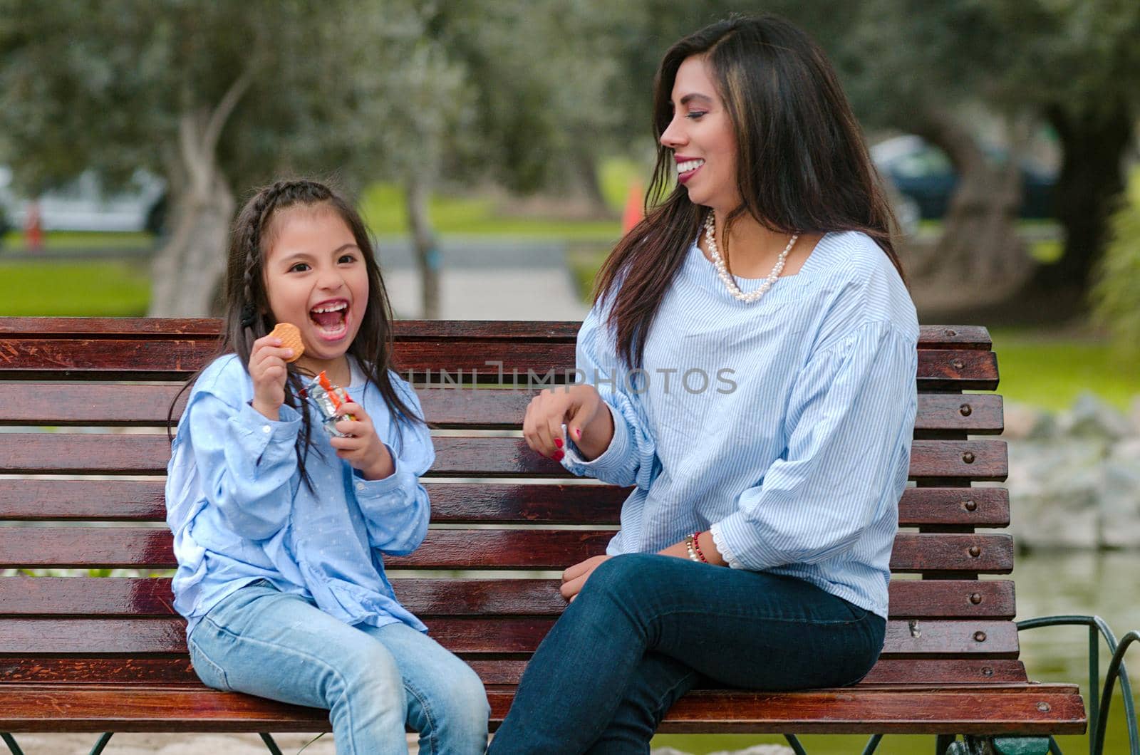 Mother and her little daughter sitting on a bench eating a cookie in the park