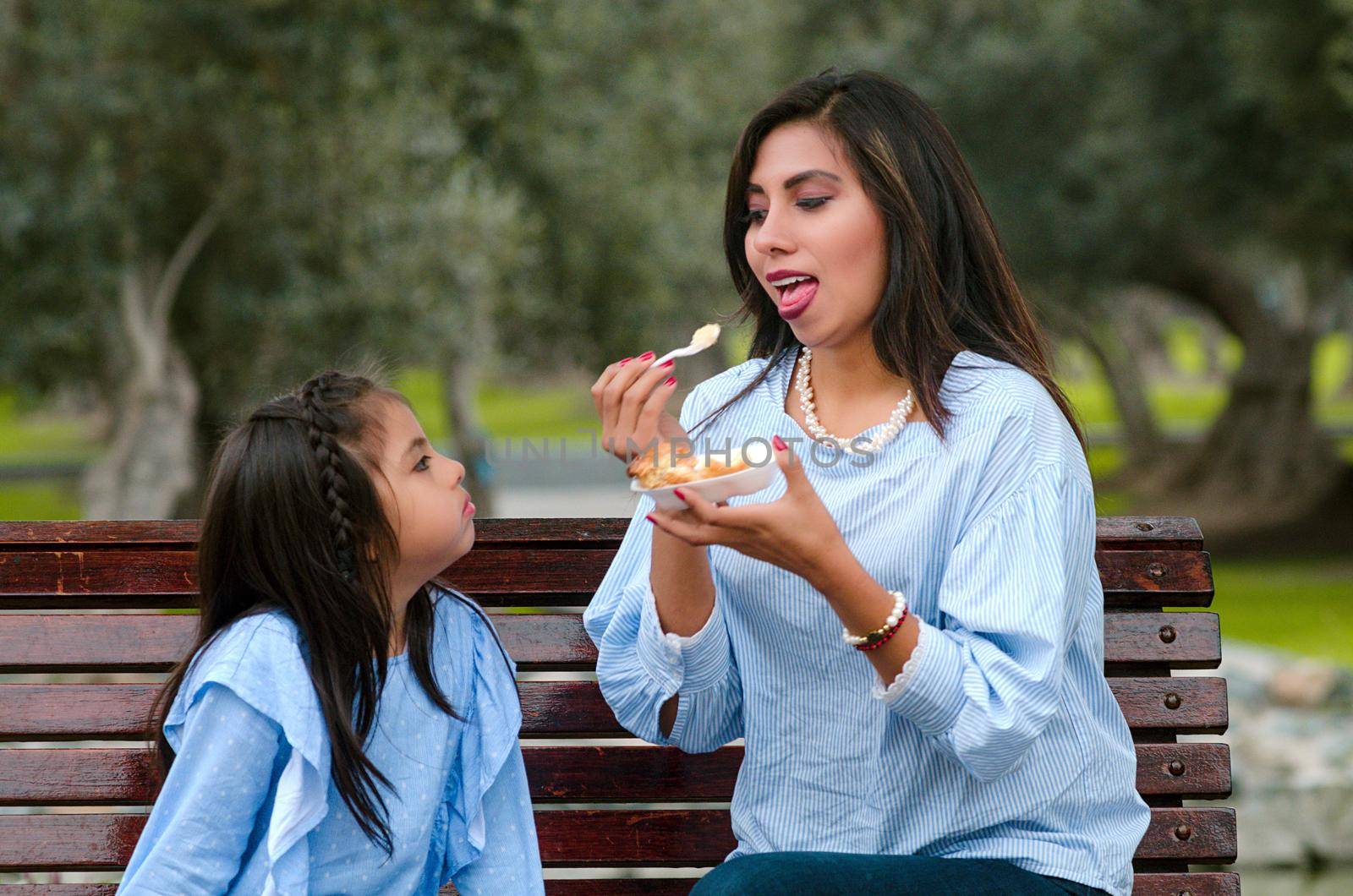 Mother and her little daughter sitting on a bench in the park eating a piece of cake