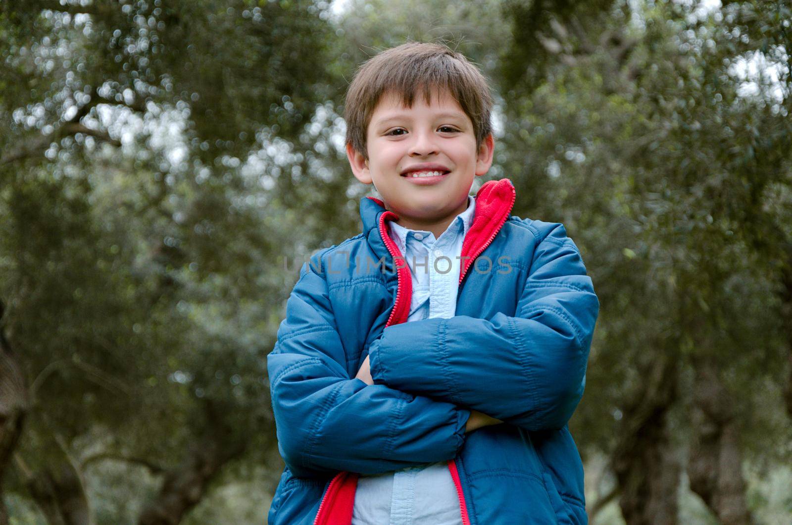 Portrait of a cute boy standing with arms crossed, smiling, looking at the camera