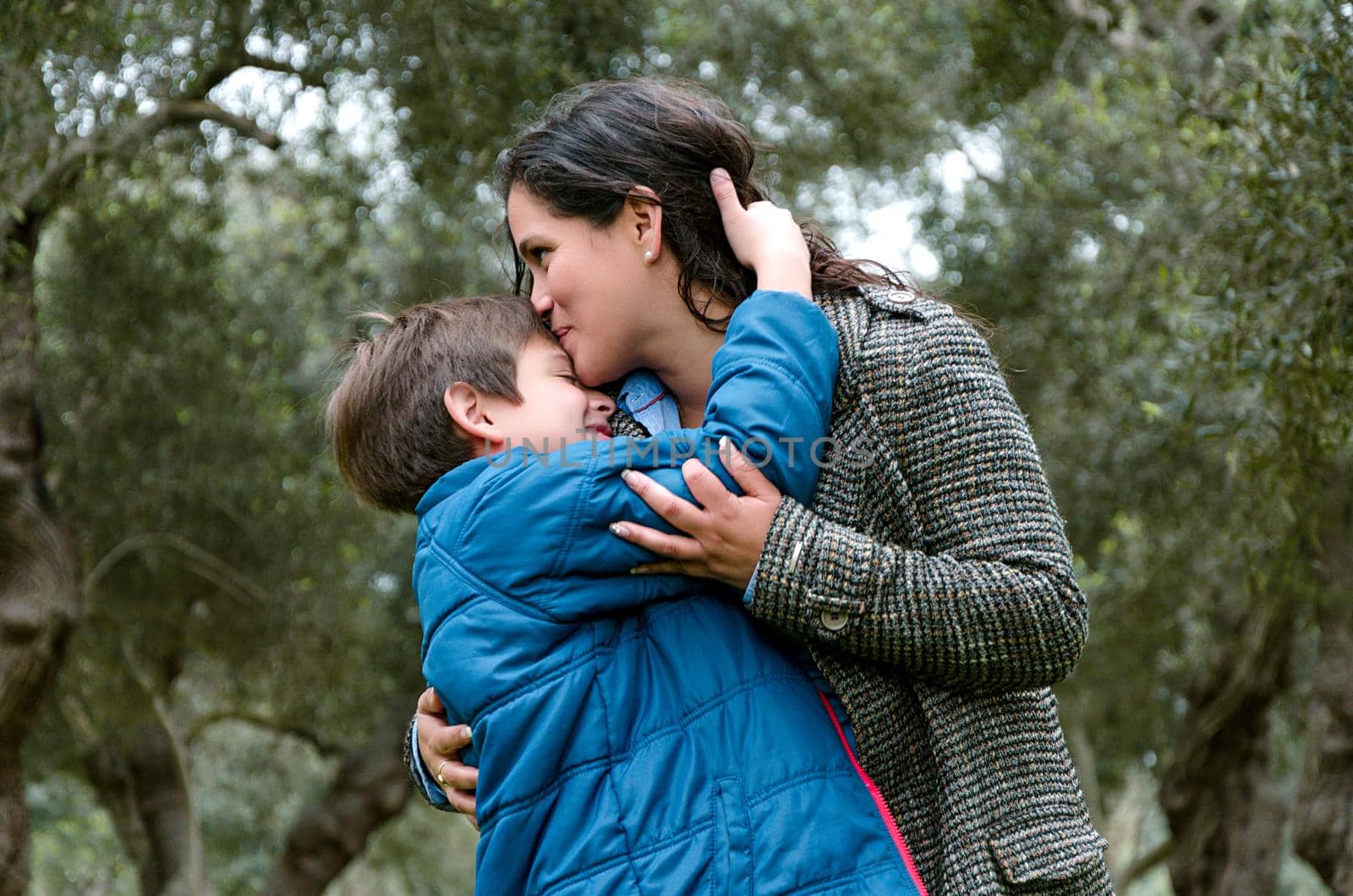 Portrait of a mother kissing her little son in the park a winter day