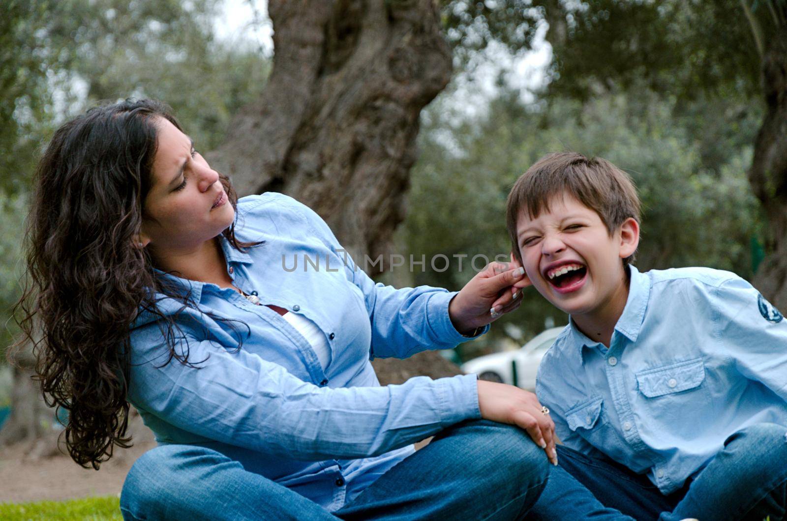 Woman scolding and pulling the ear of the scared young boy